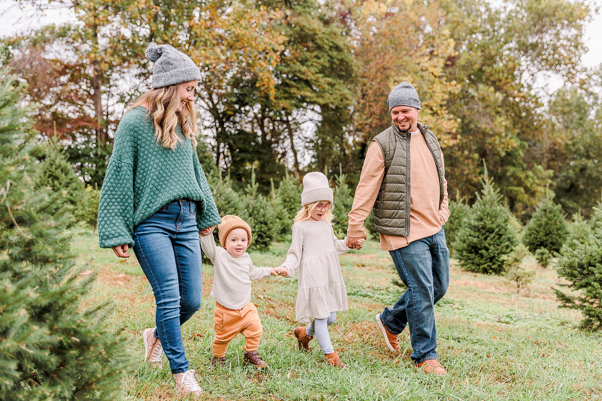 parents hold kids' hands walking during portraits at Christmas tree farm
