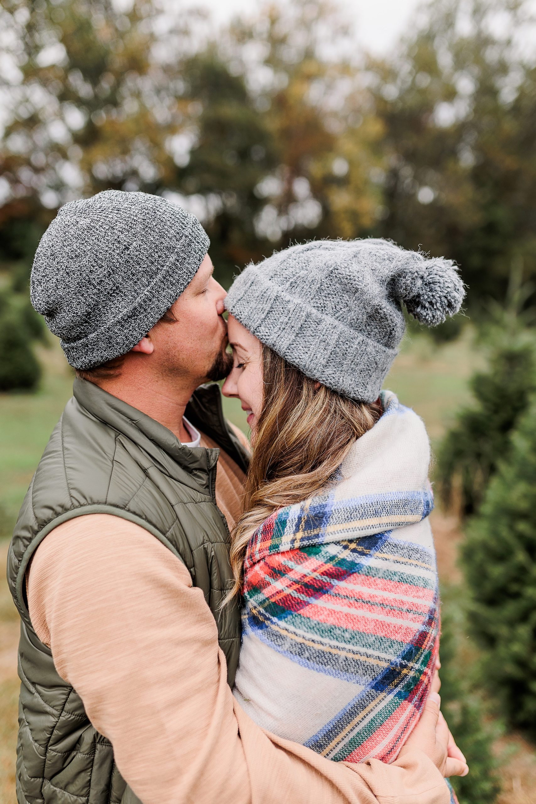 husband kisses wife's forehead during Christmas tree farm portraits