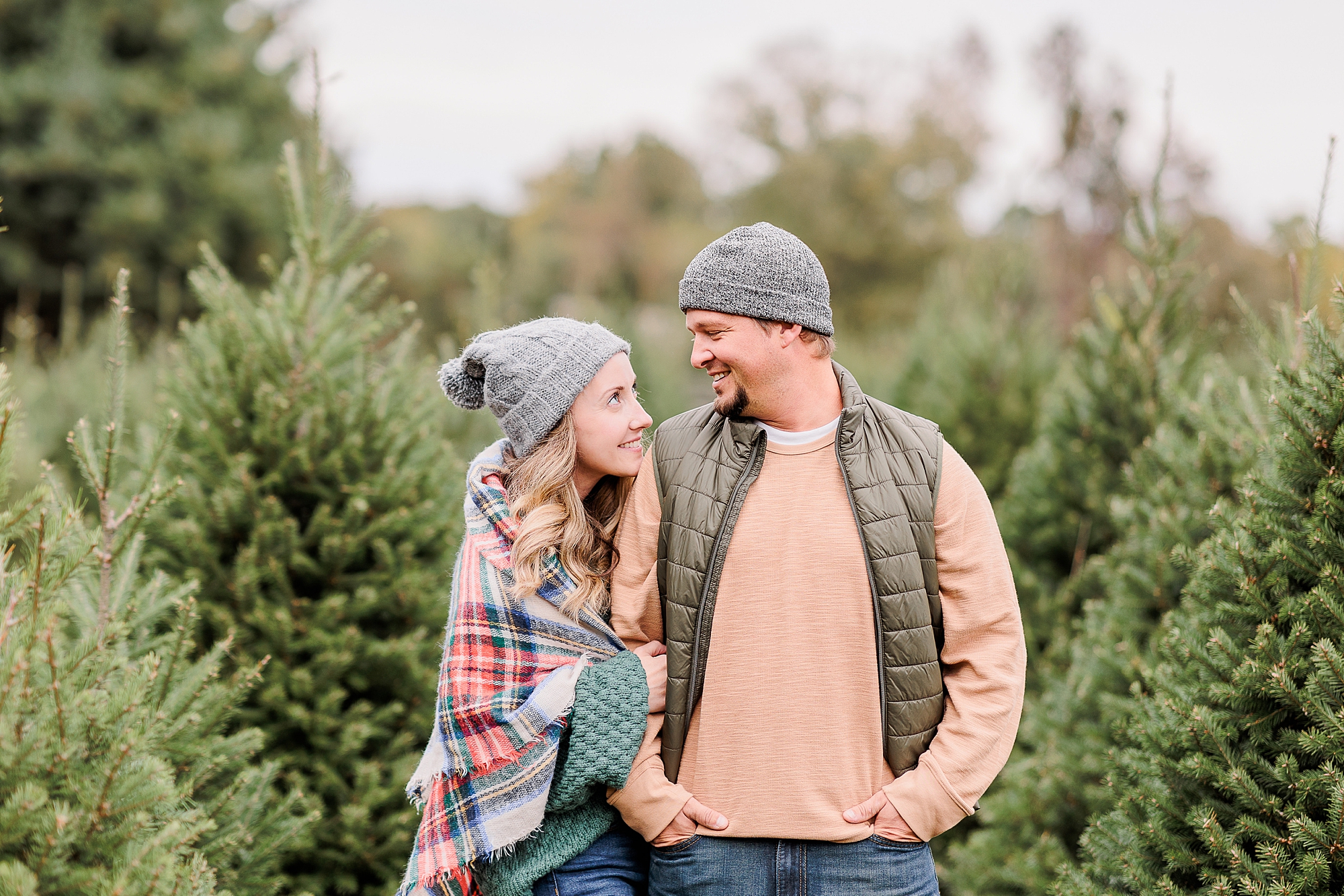 couple hugs between trees during Maryland Christmas tree farm portraits