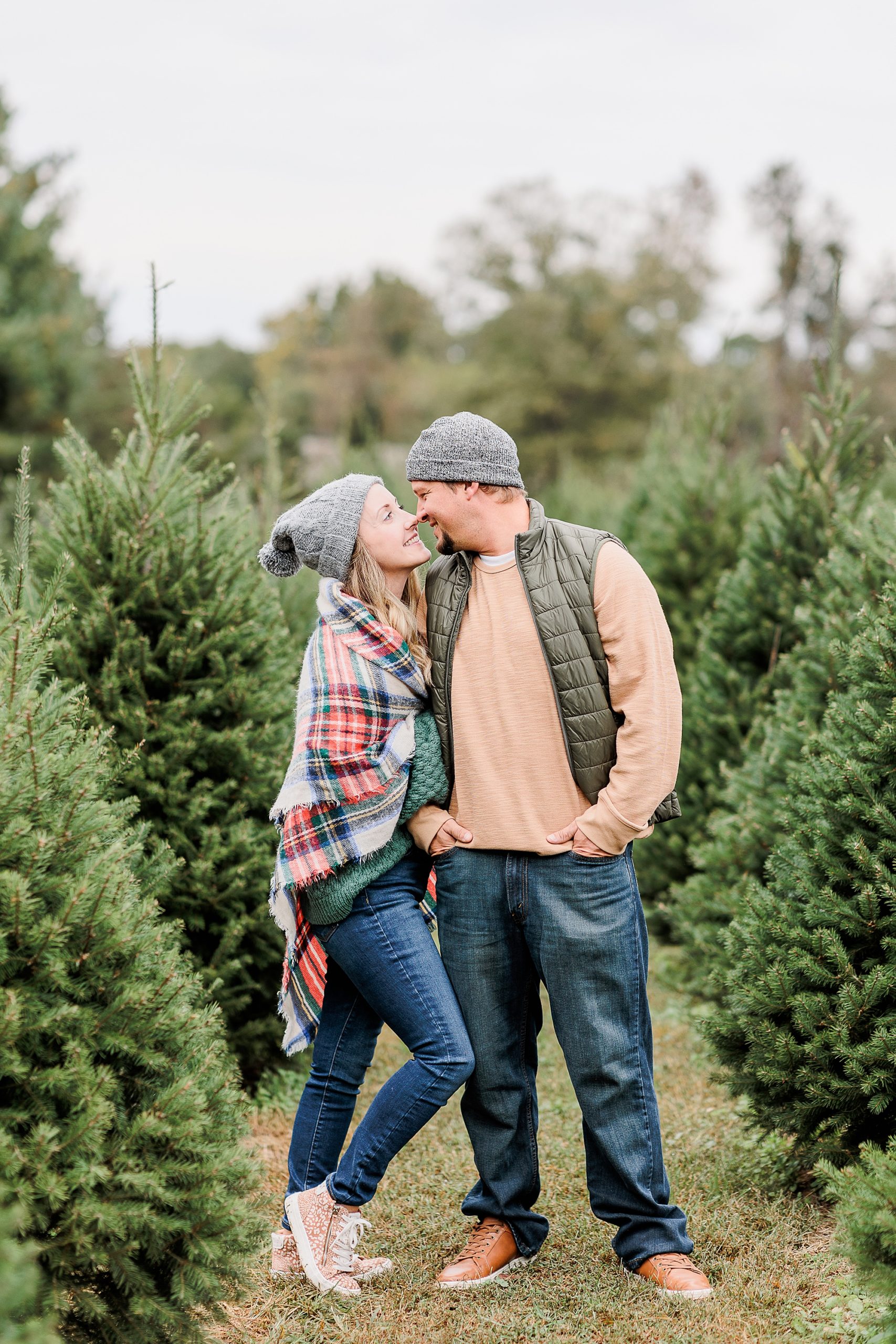 couple hugs between rows of trees during Christmas tree farm portraits