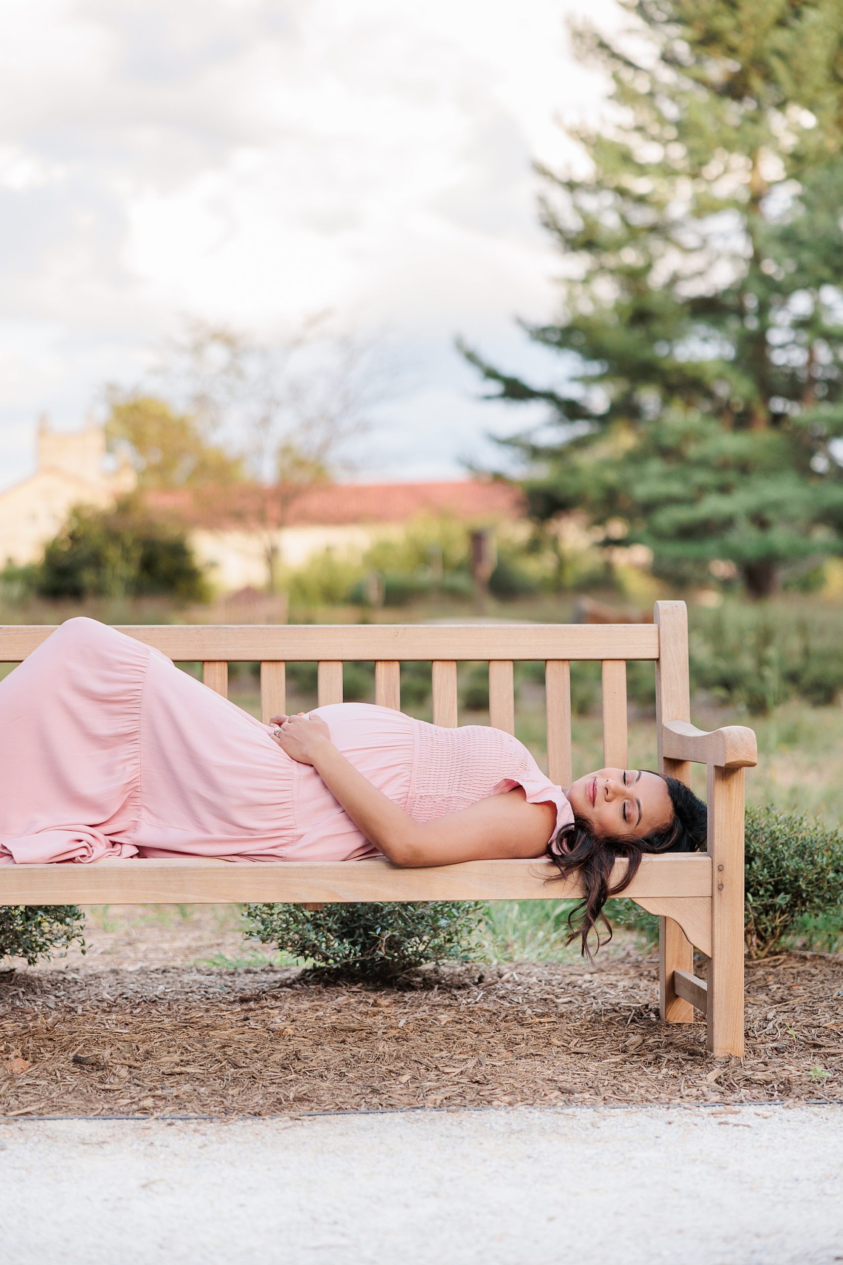 expecting mother in pink dress lays on wooden bench in Maryland 