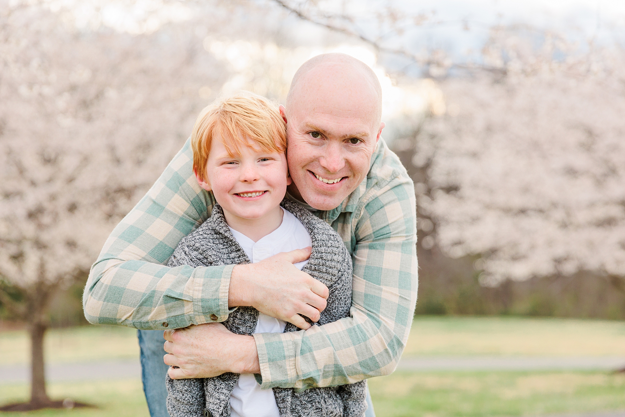 dad hugs son in front of cherry blossoms during family photos