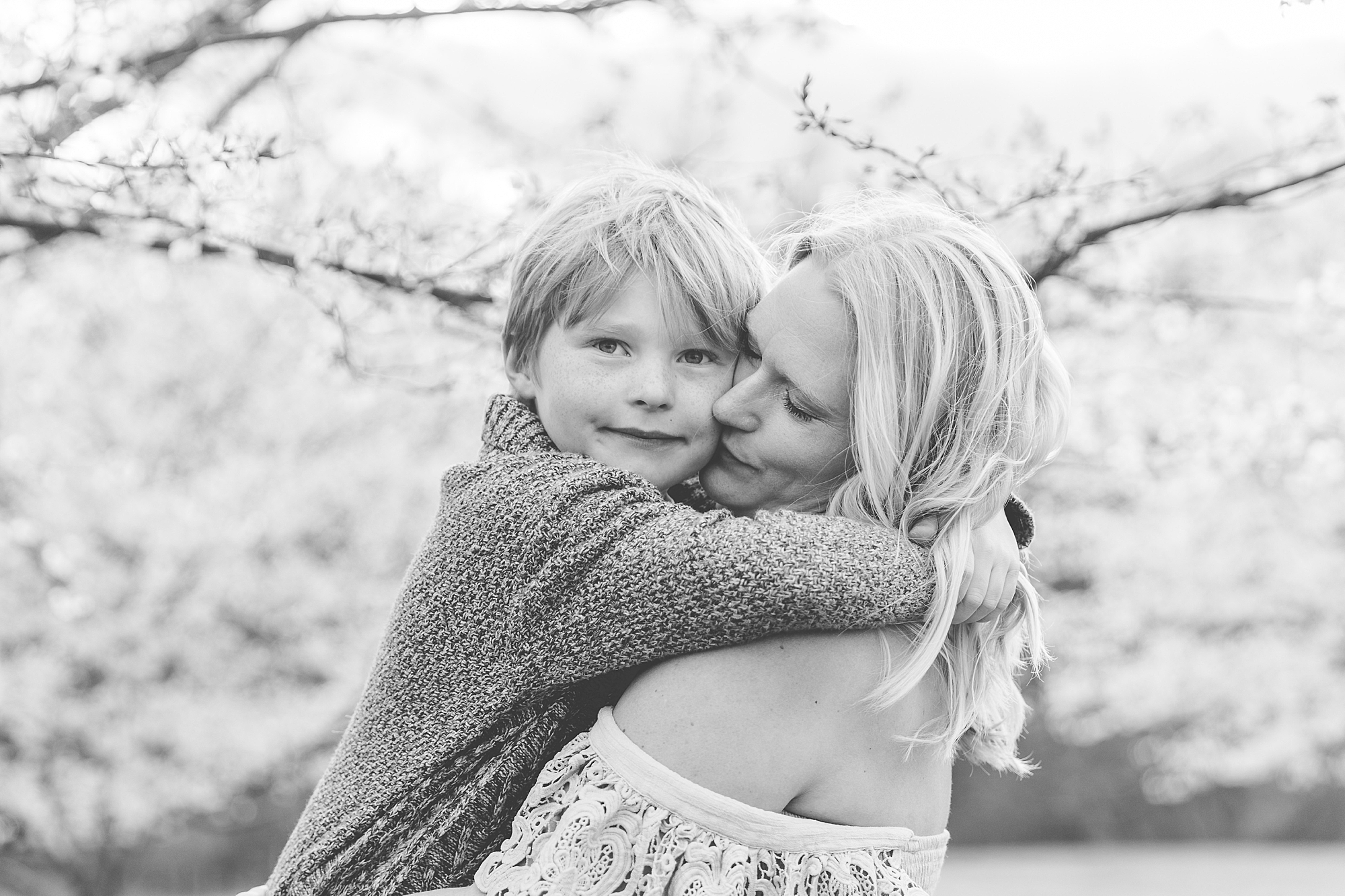 mom hugs son during family portraits in cherry blossoms 