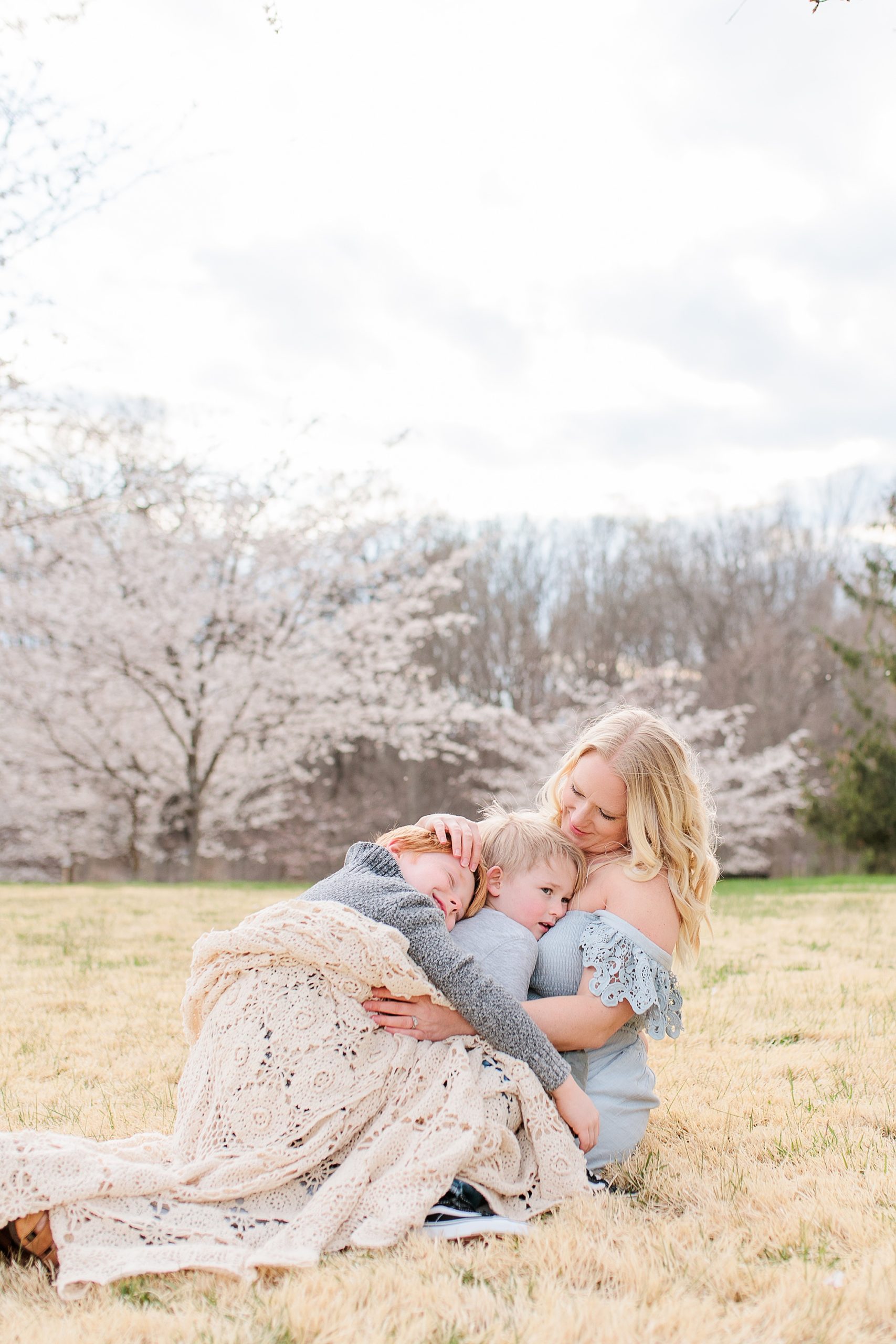 mom in blue gown hugs son in front of cherry blossoms