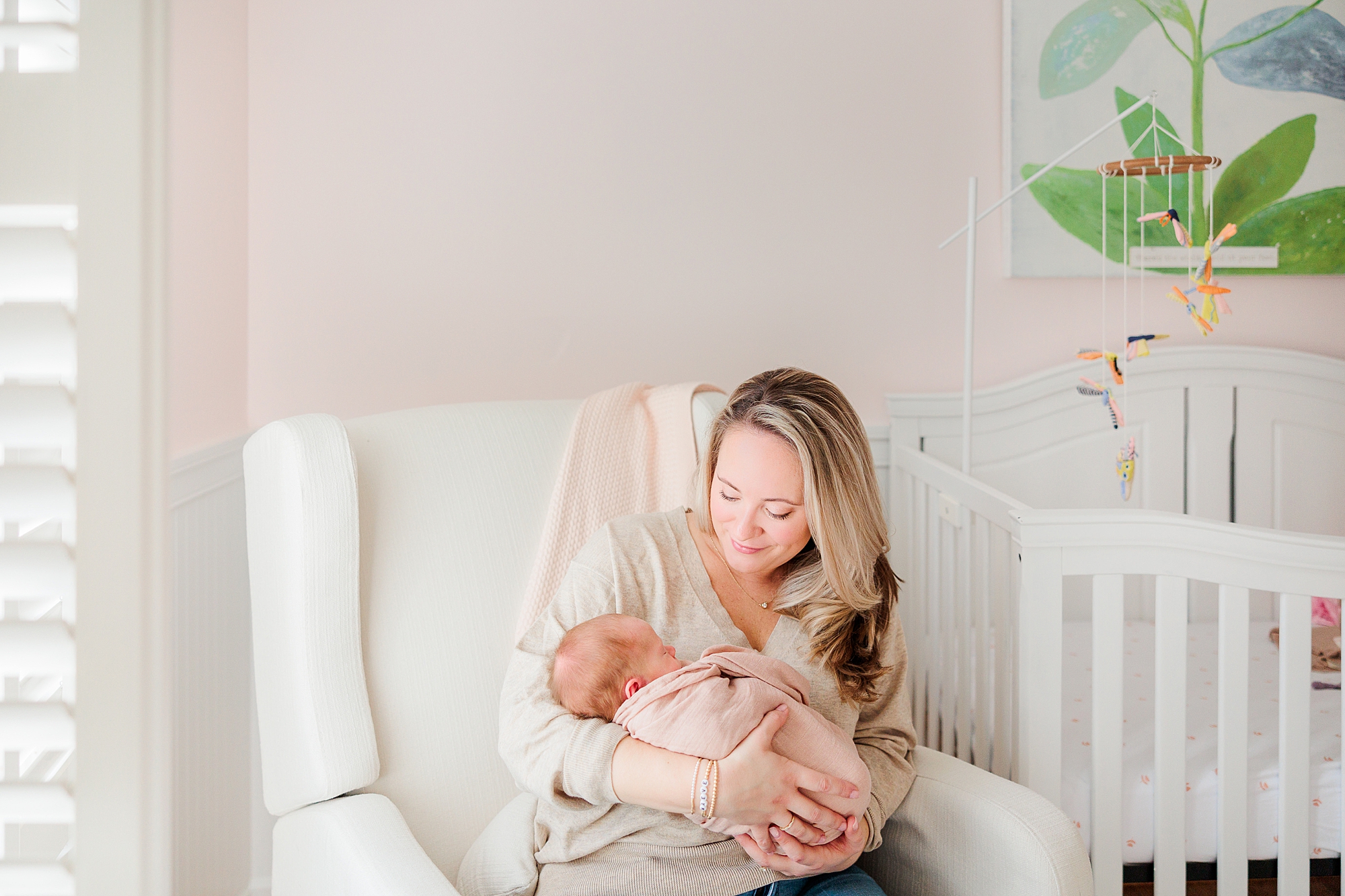 mother holds daughter in pink blanket in nature inspired nursery