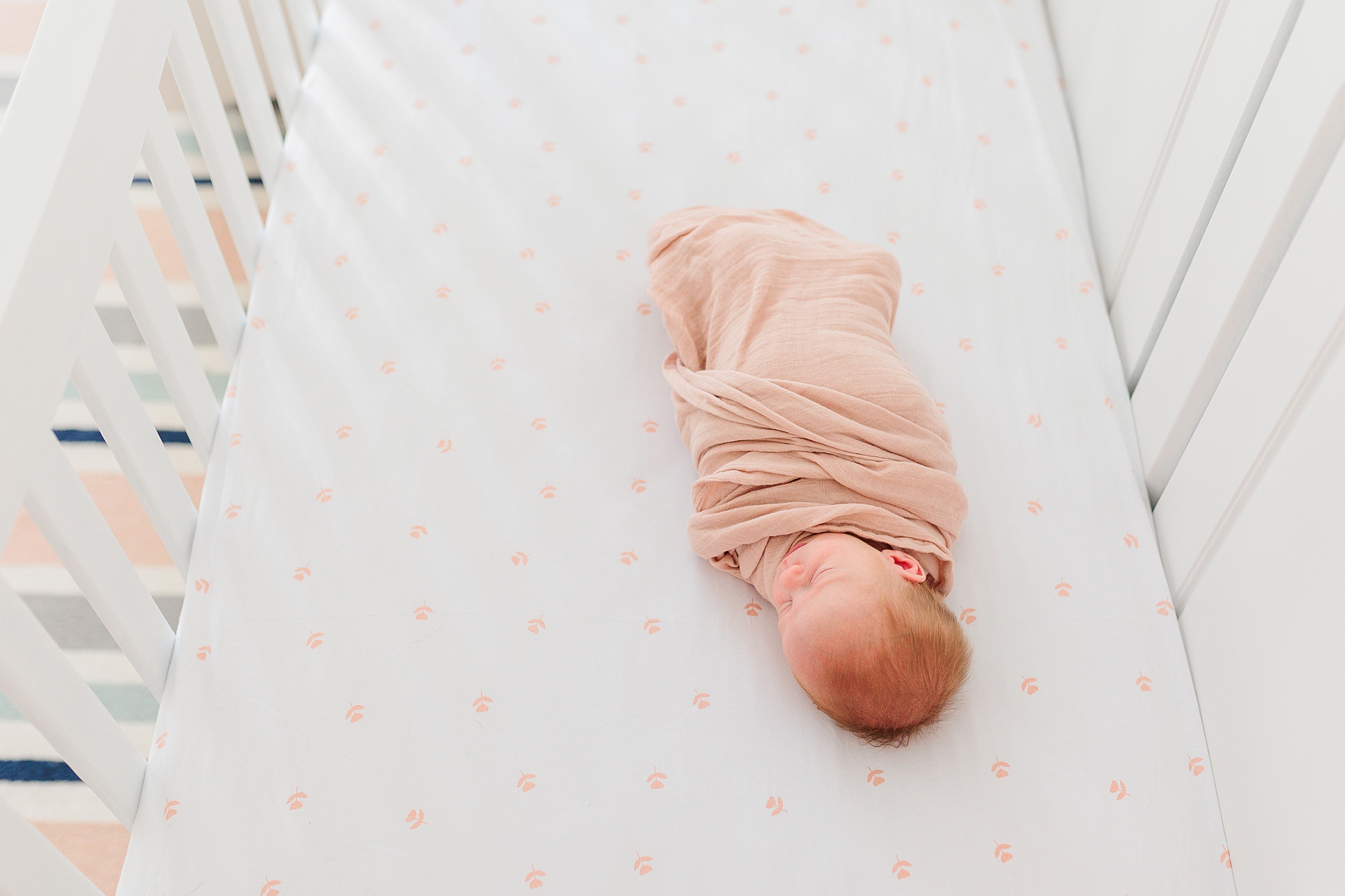 baby girl in pink blanket lays on white sheets in nature inspired nursery