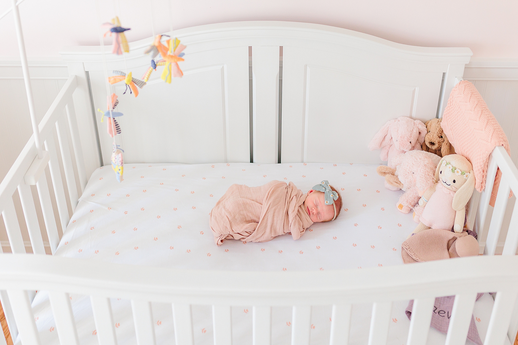 baby girl lays in white crib in pink blanket during newborn session 