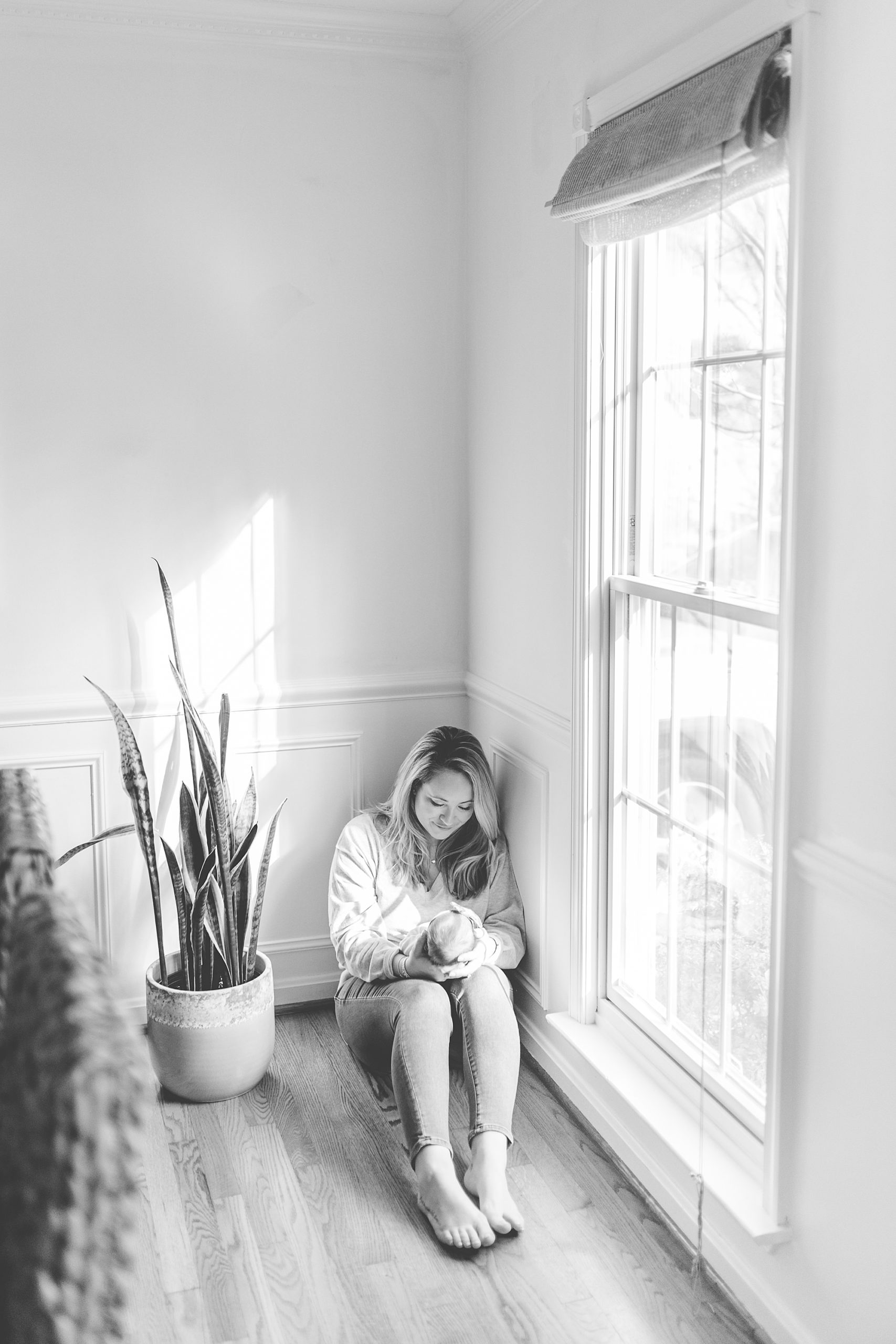 mom holds daughter sitting by window in home during lifestyle newborn photos 