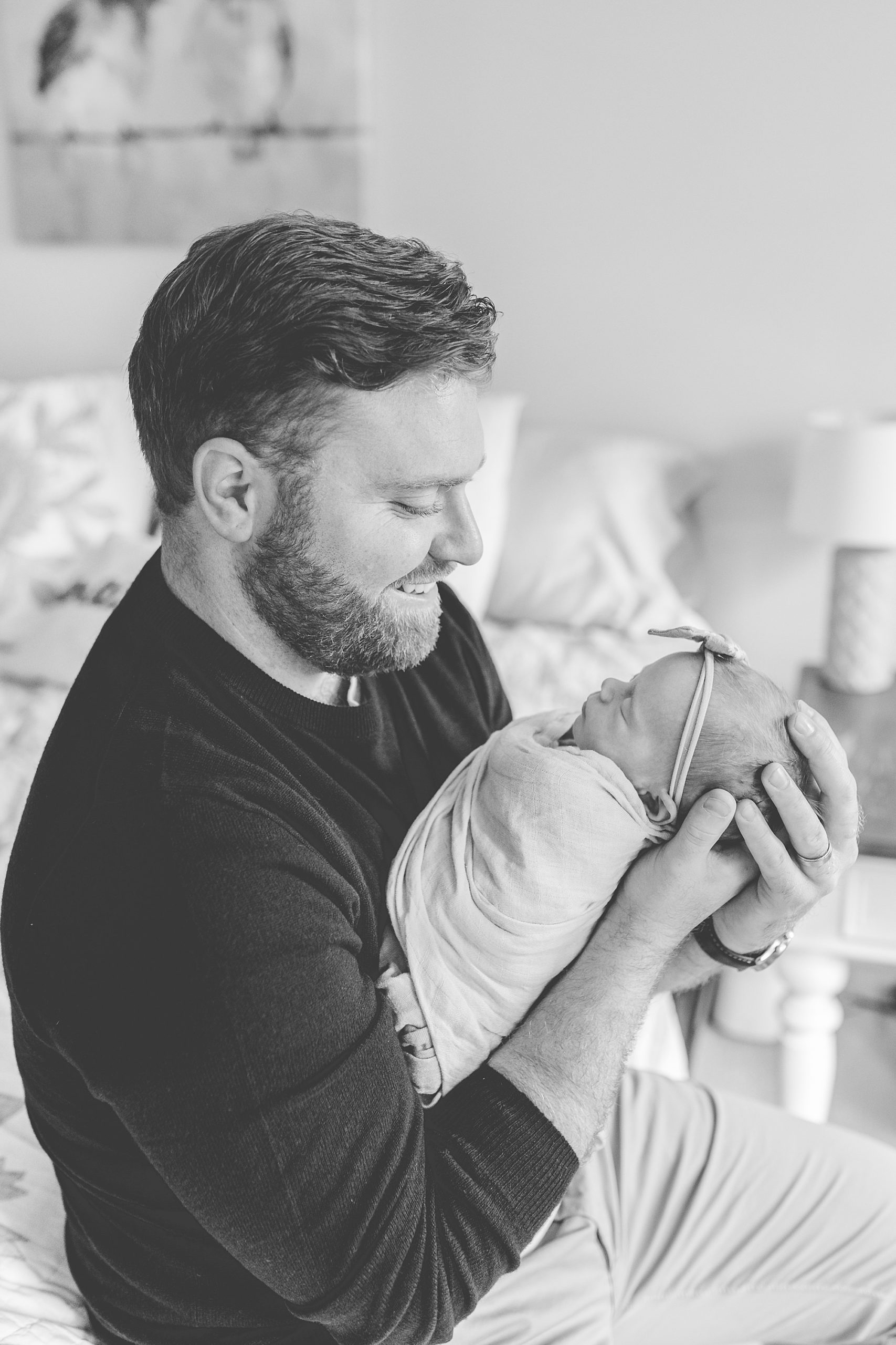 dad holds newborn daughter against chest during newborn photos at home 