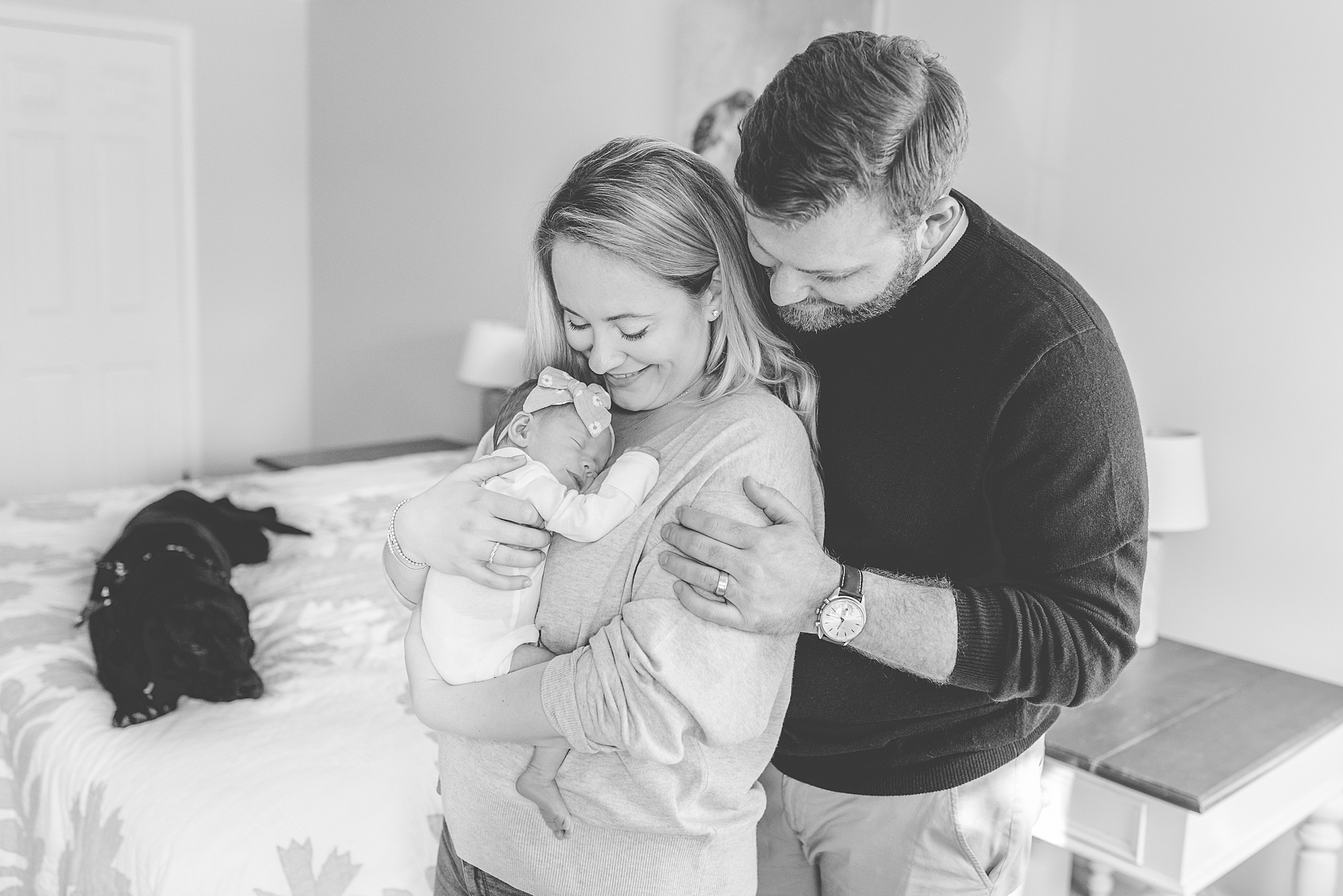 husband hugs wife from behind while she holds daughter 