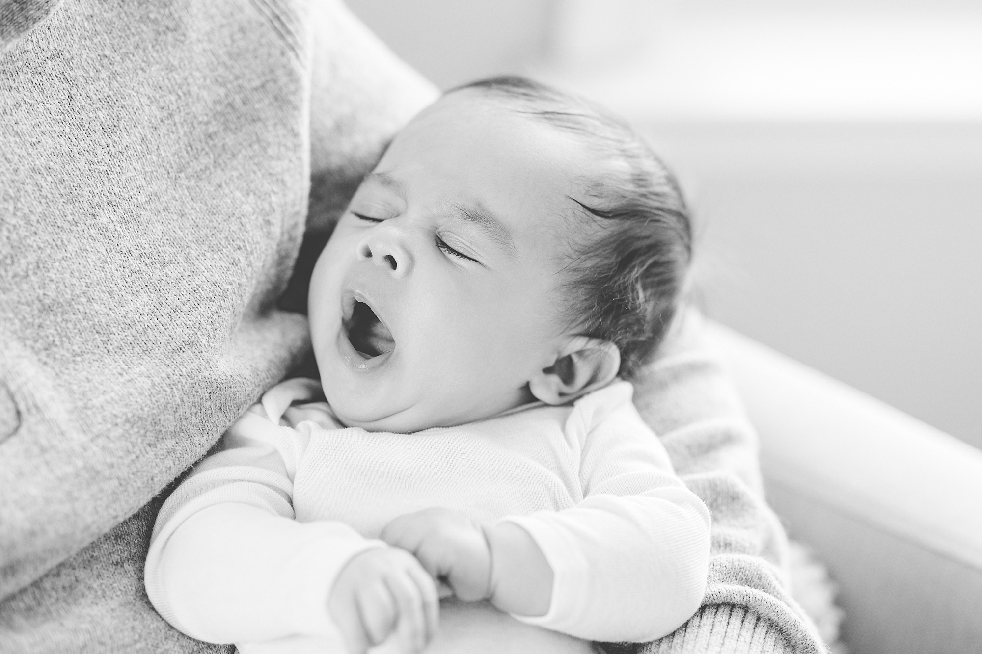 black and white portrait of baby yawning in white onesie