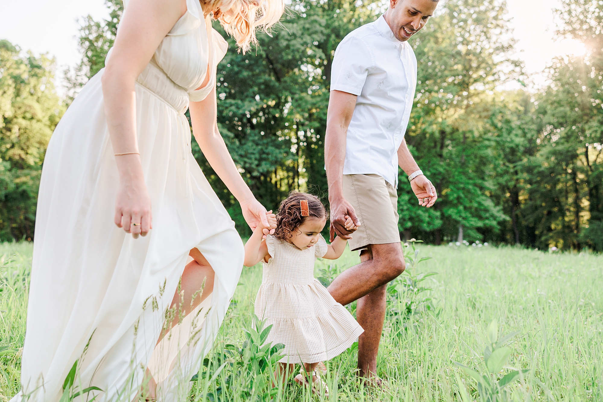 mom and dad walk with toddler in cream dress through peony field 