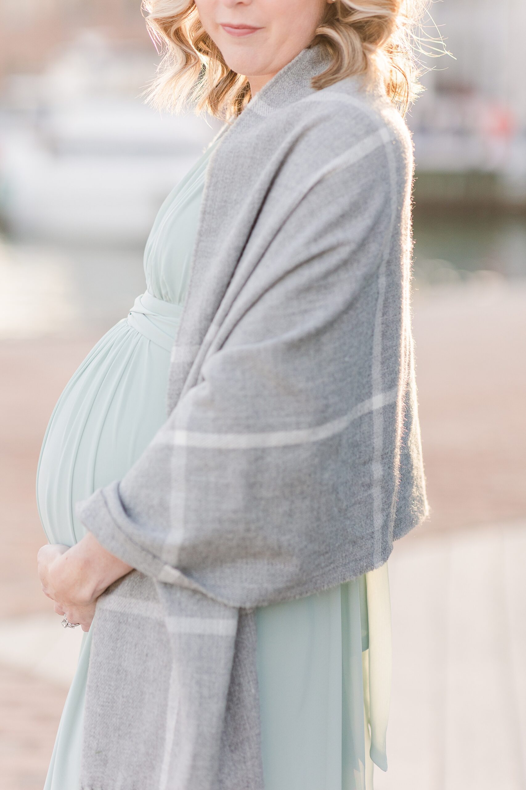 woman holds baby belly in green dress with grey shawl