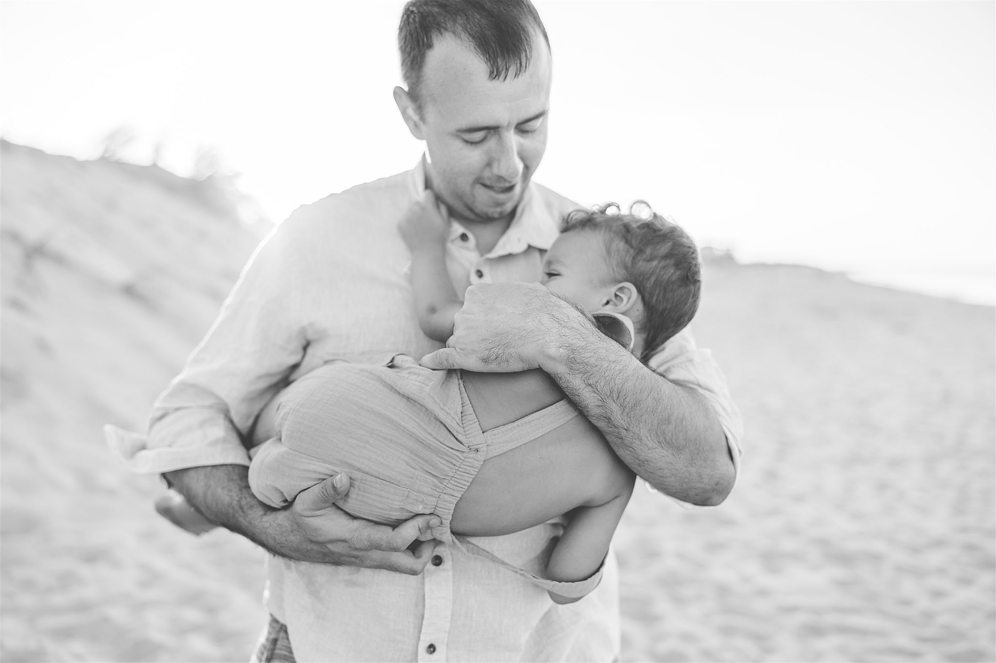 dad snuggles toddler son on beach 