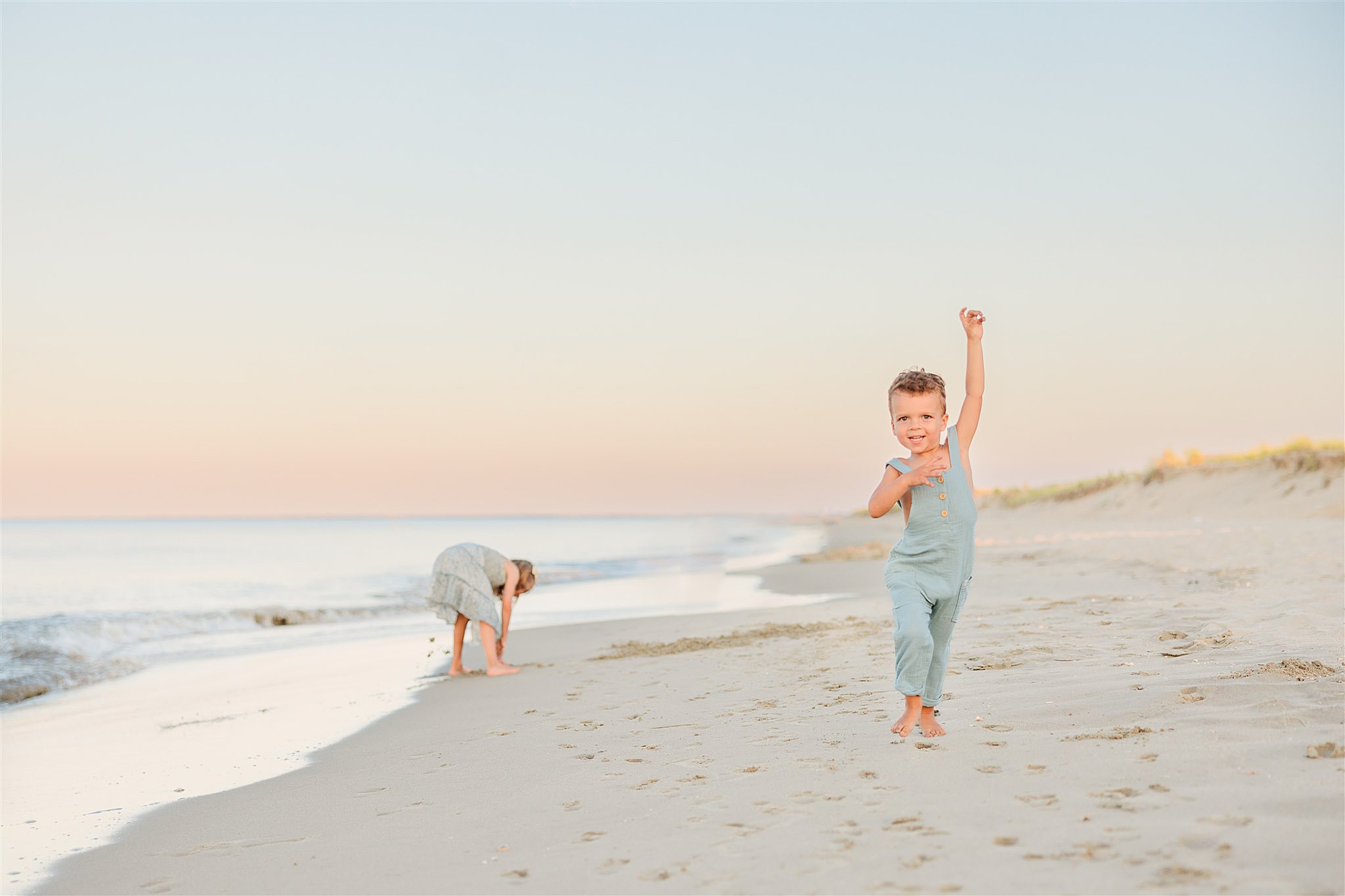 toddler boy jumps while sister picks up seashells