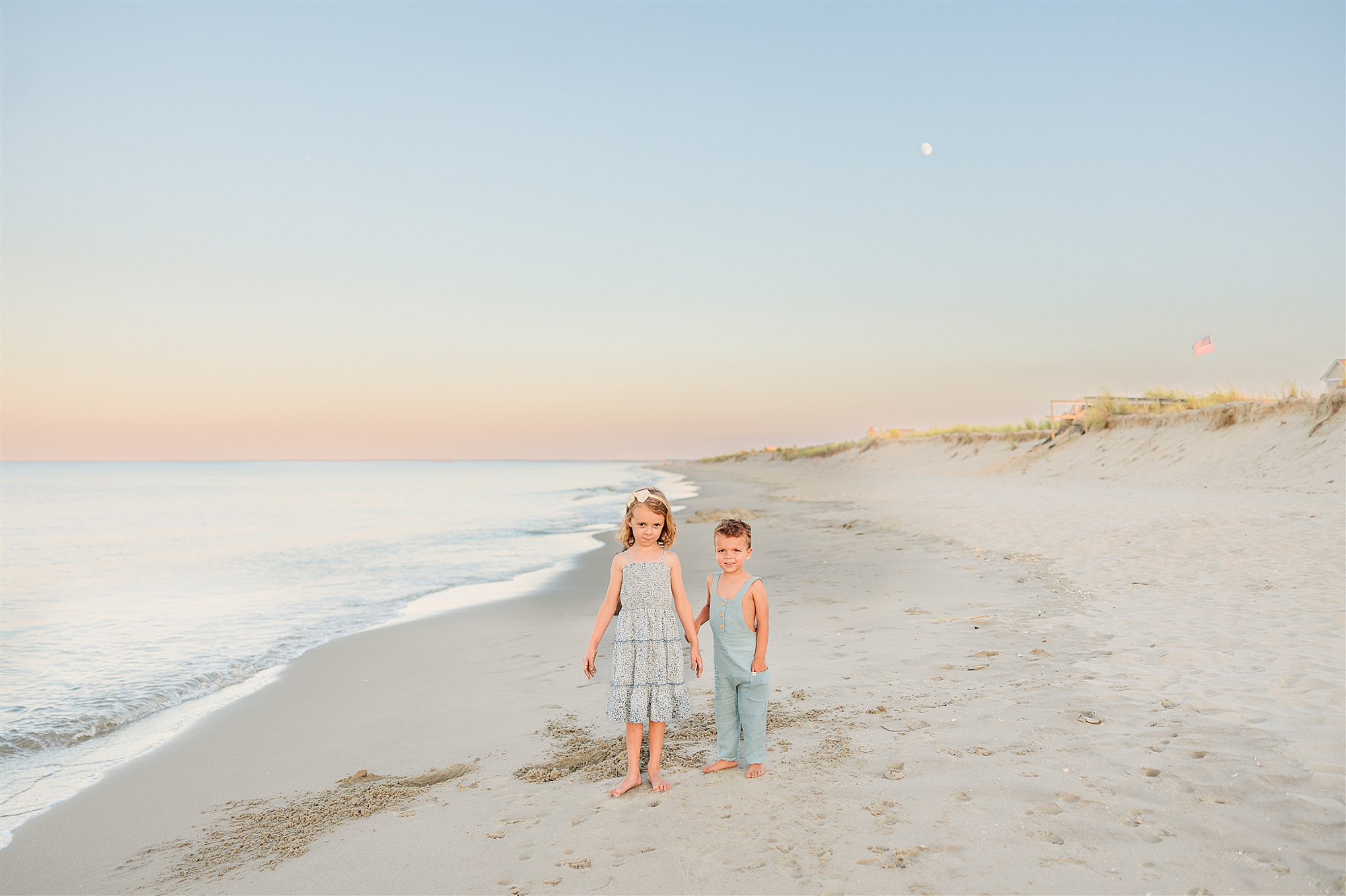 sister and brother hold hands walking on beach in Delaware 