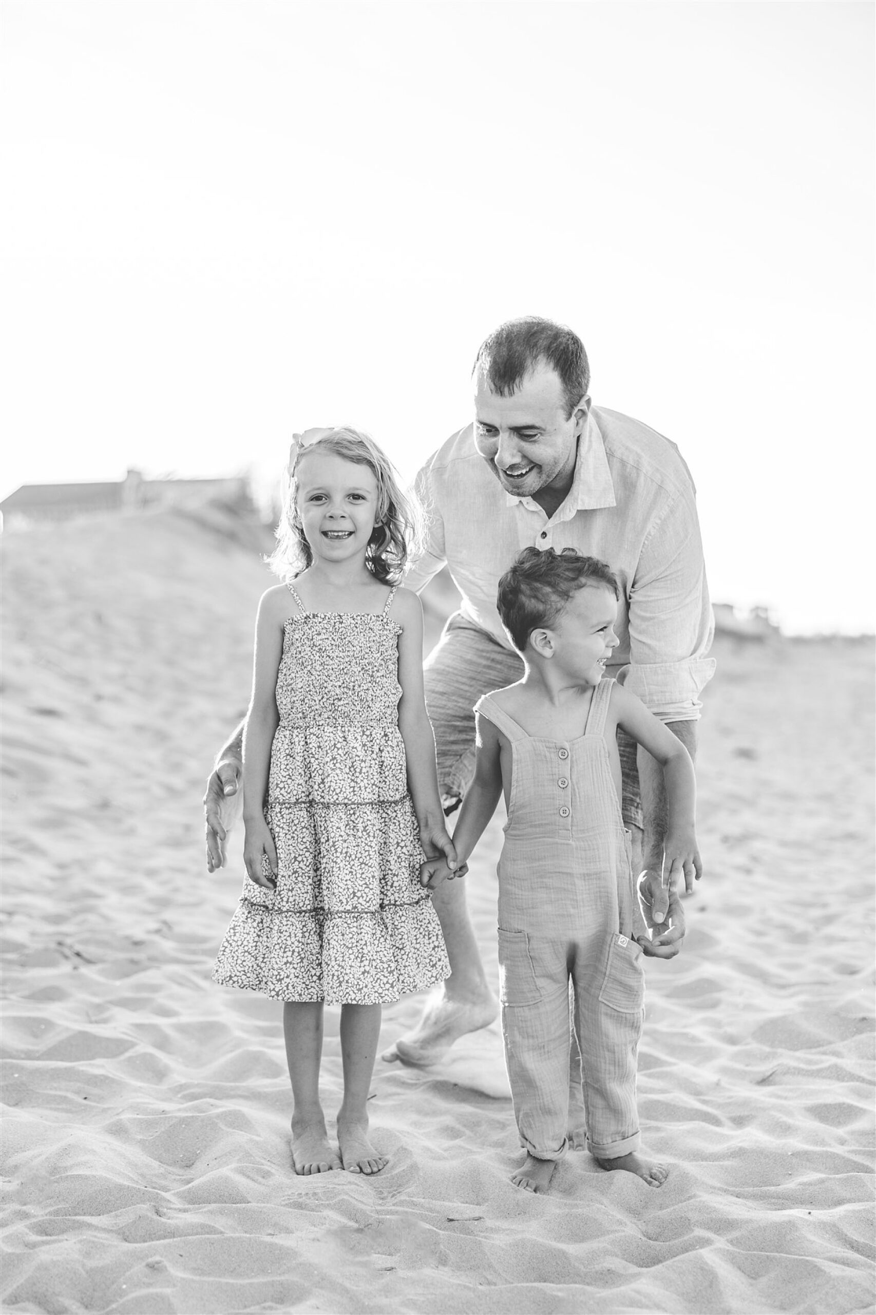 dad poses behind toddlers during photos at sunset on Delaware Beach