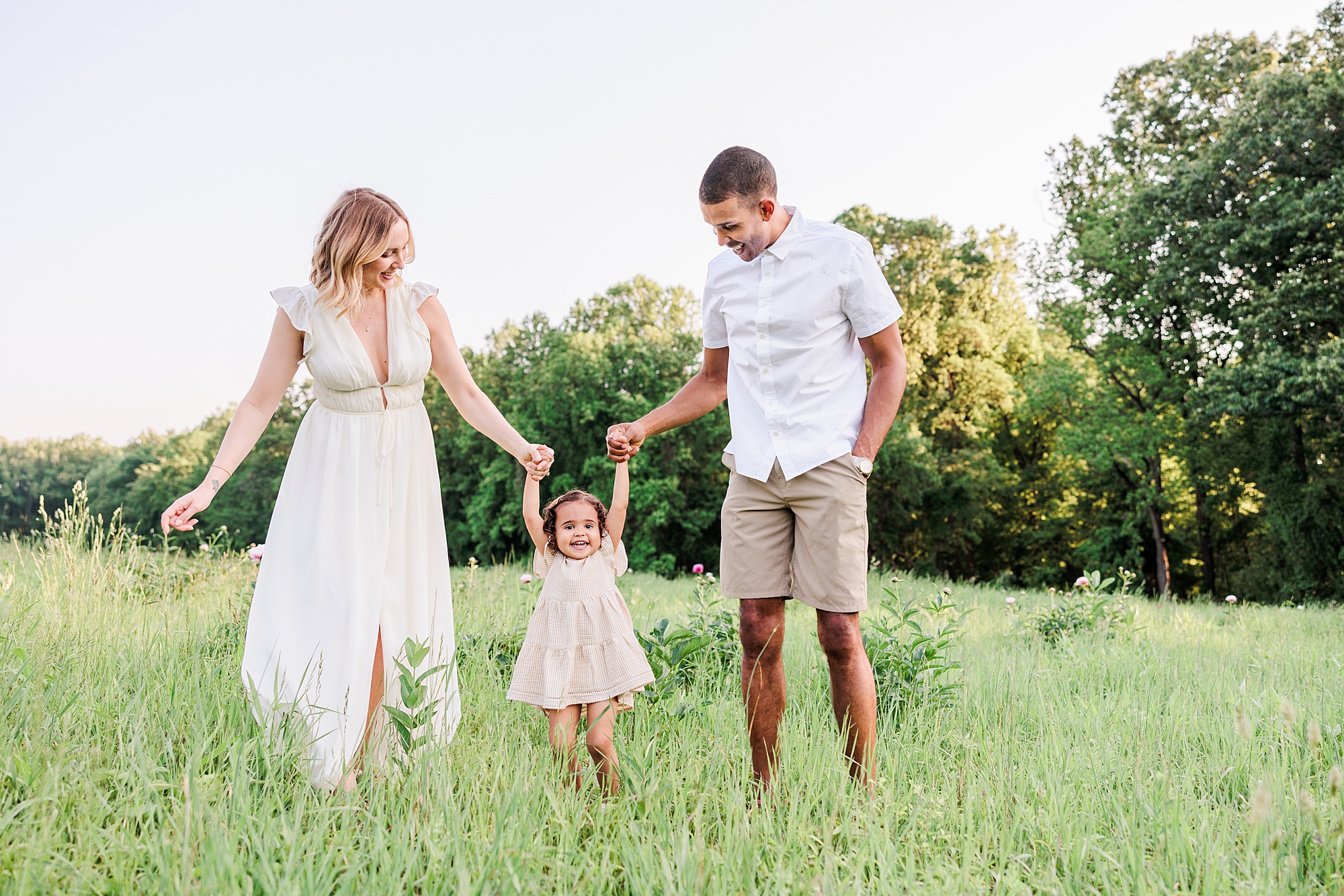 family of three walks through field in neutral spring outfits
