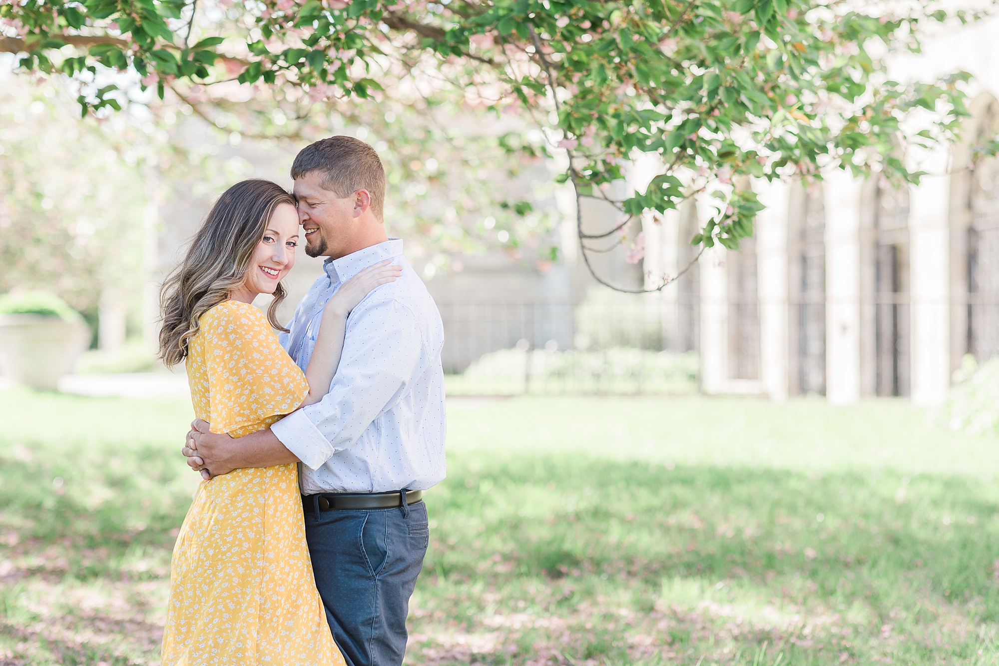 couple hugs under tree in yellow and blue spring outfits 