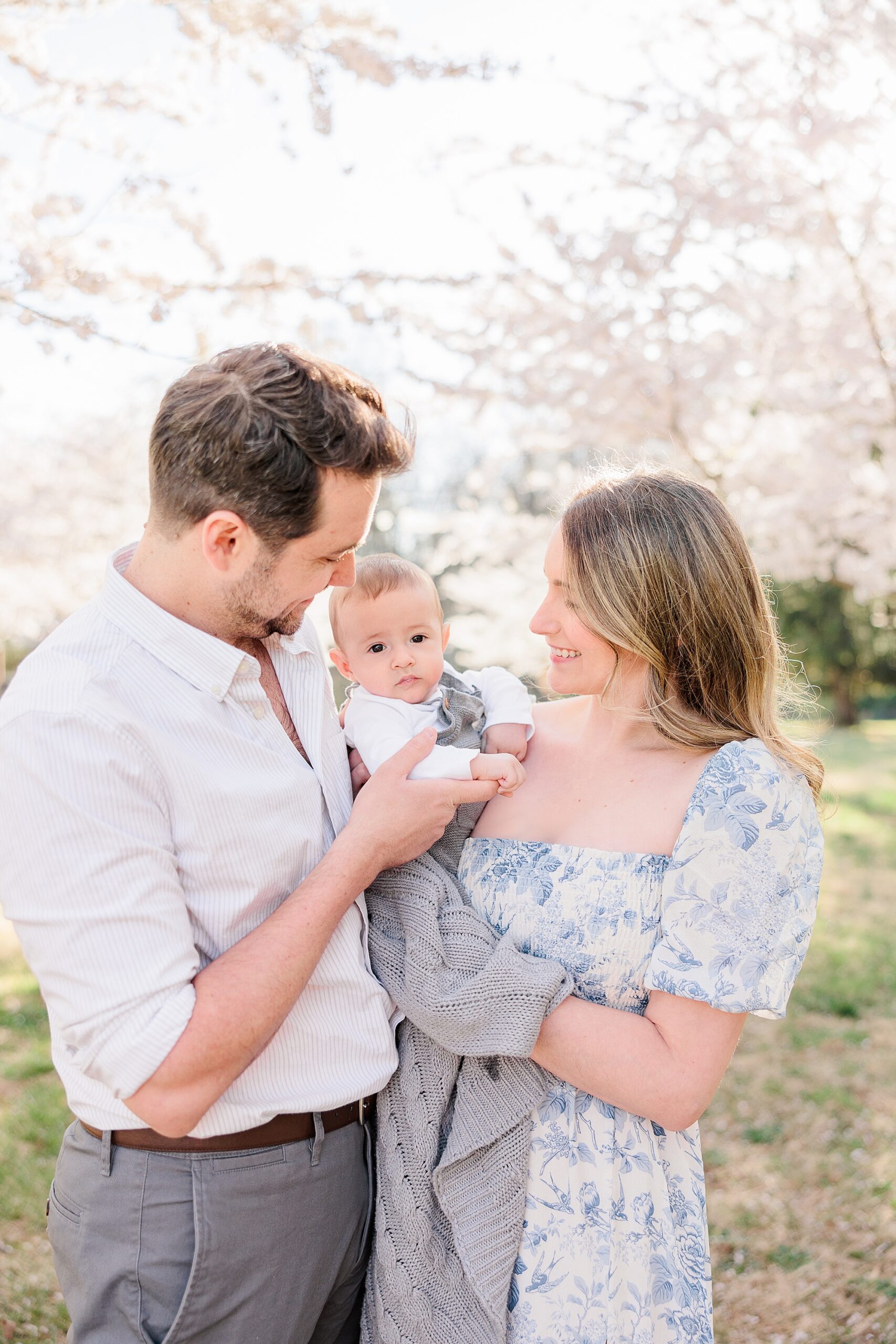 couple holds baby between them under cherry blossoms