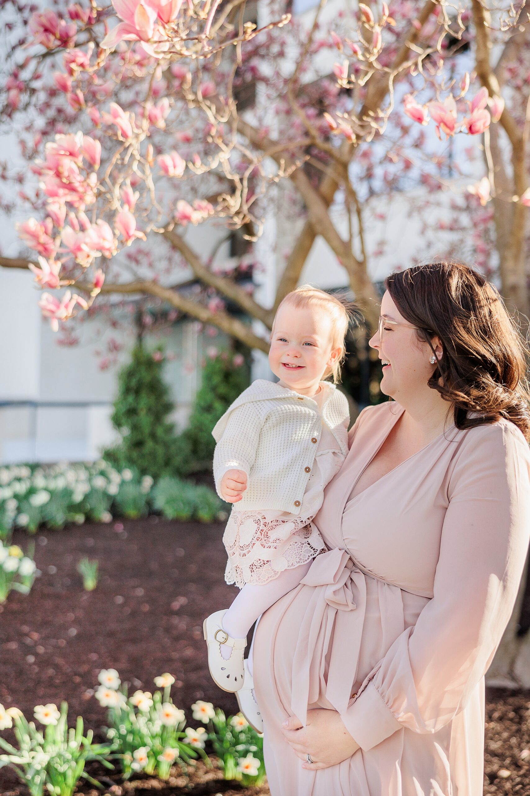 expecting mom in pink gown holds toddler on her hip 