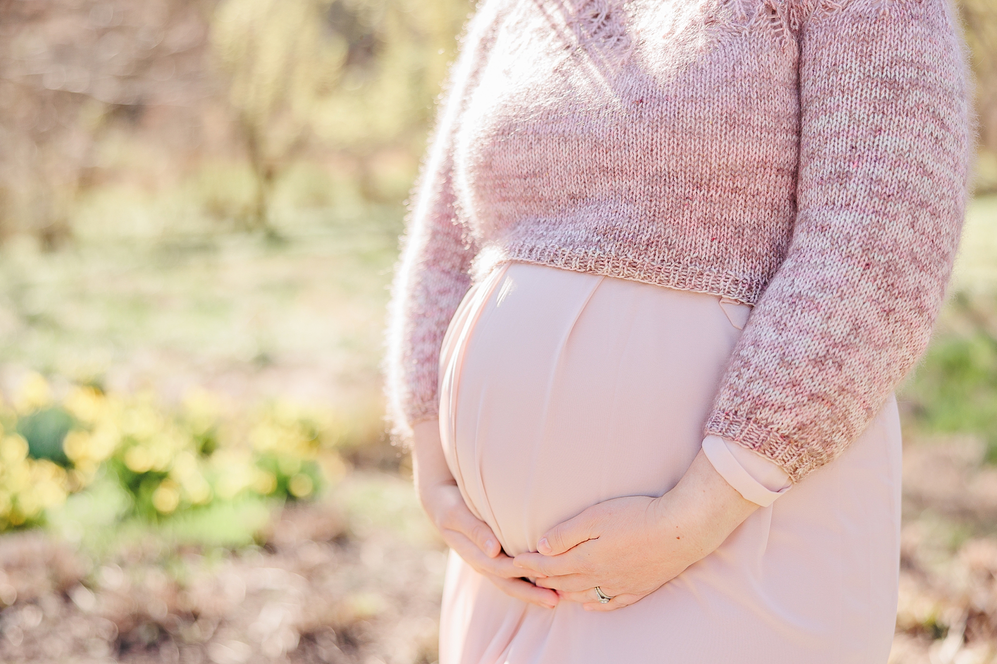 expecting mom holds baby bump in pink gown with knit sweater