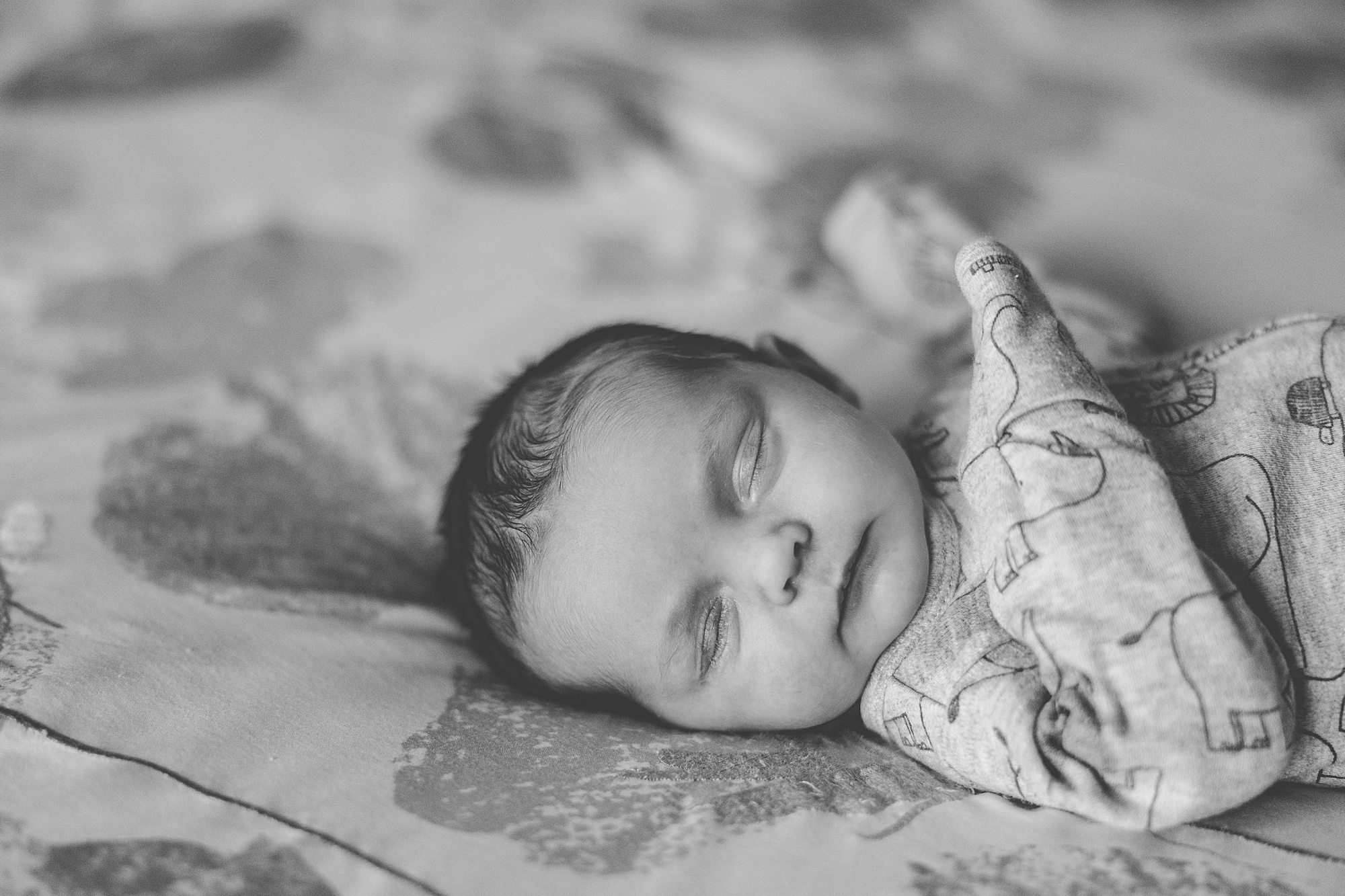 baby lays sleeping on floral bedspread during newborn photos at home 