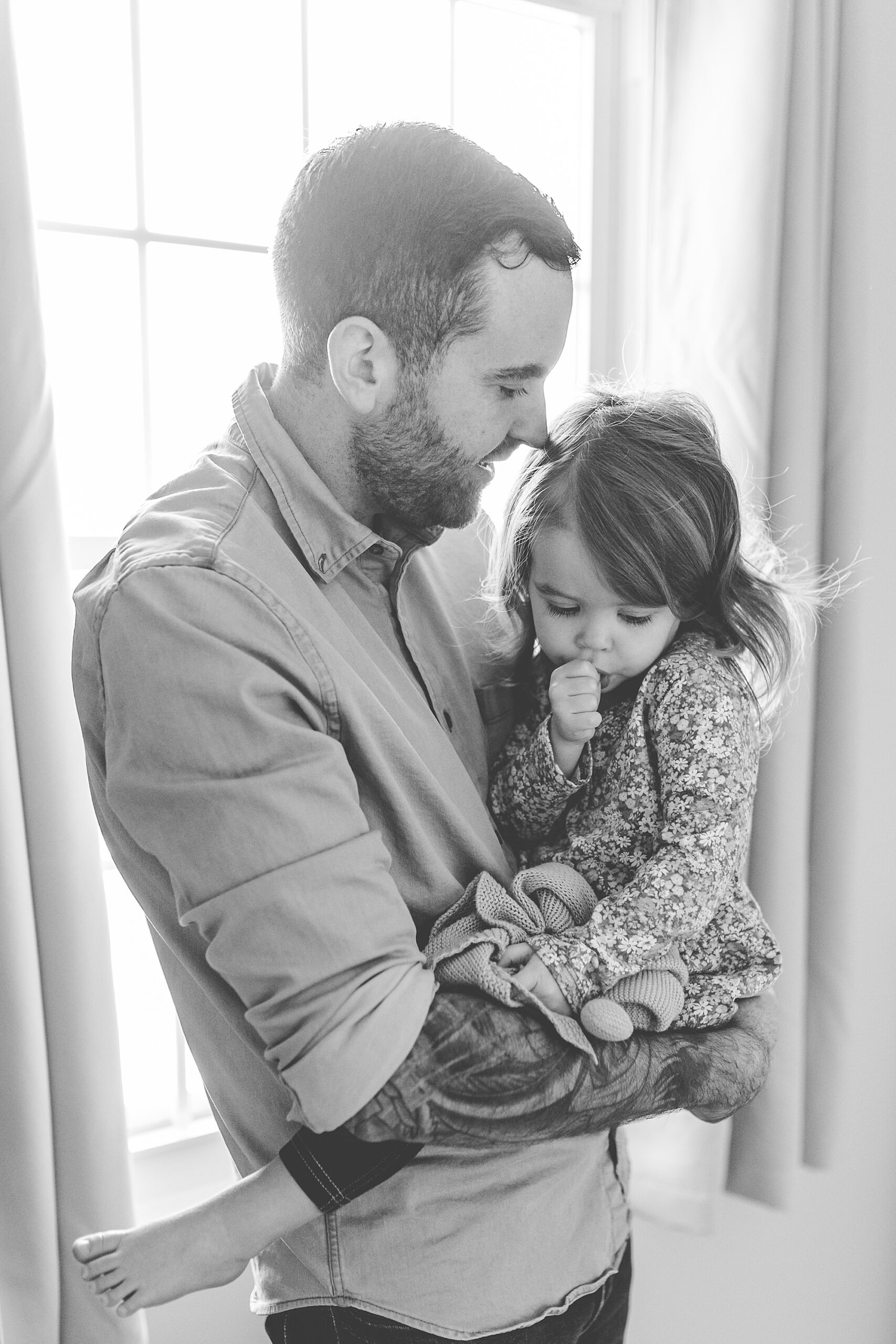 dad holds toddler daughter in window during lifestyle photos at home 