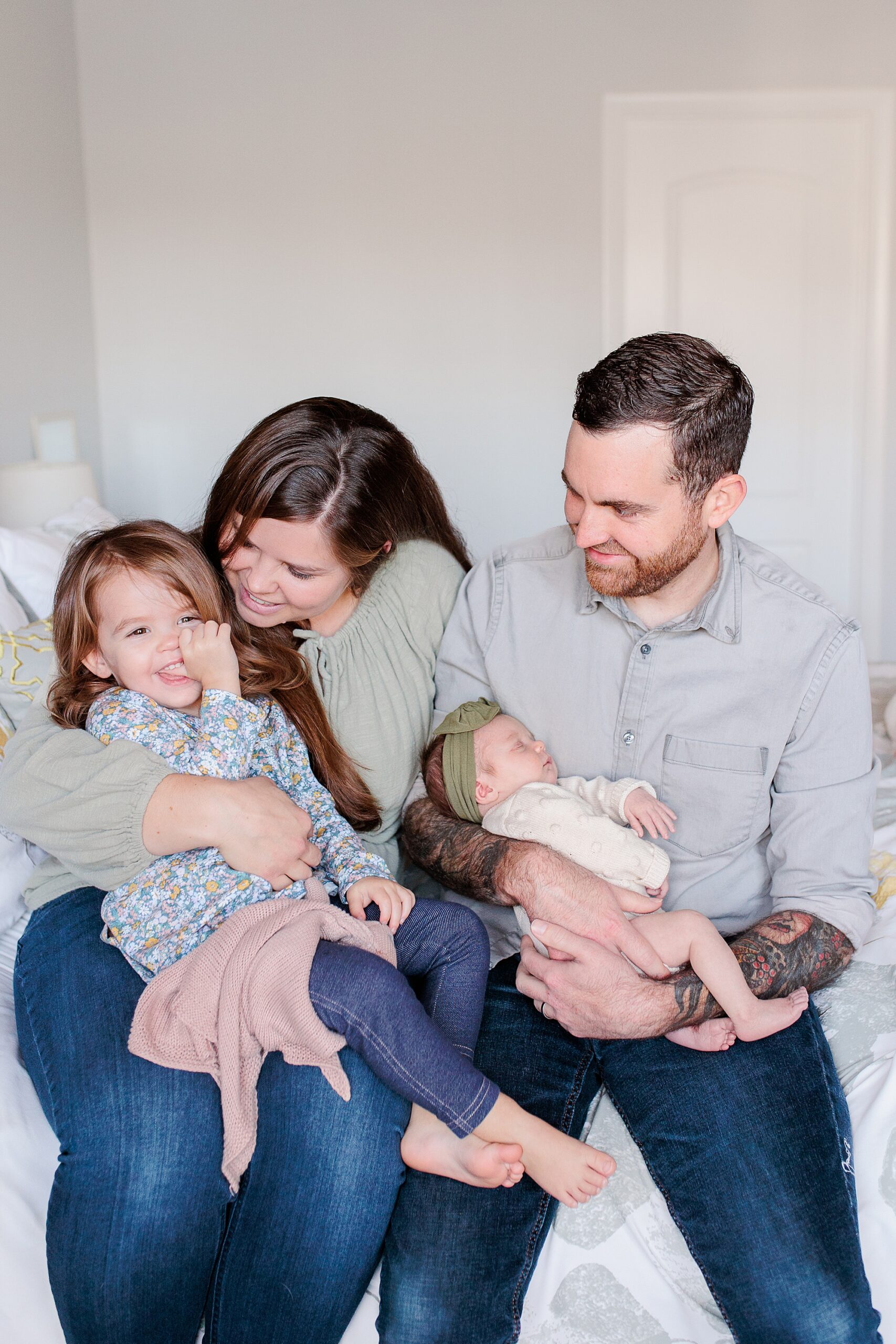 parents hold daughters sitting on bed during Maryland newborn lifestyle photos