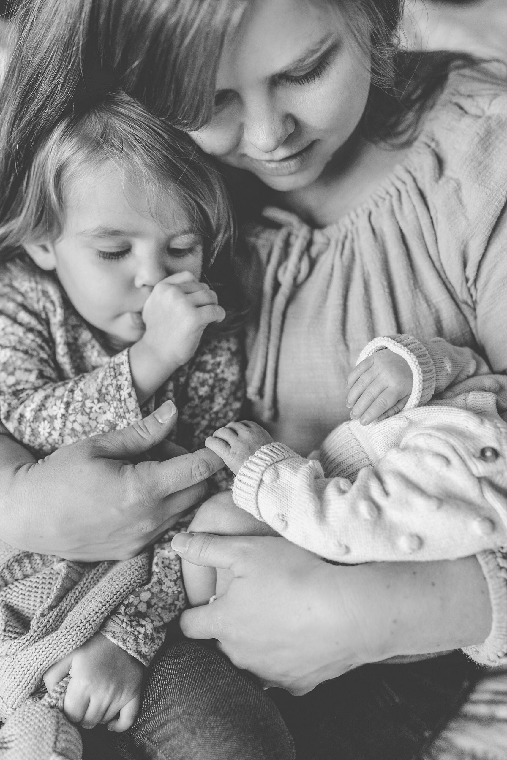 toddler sucks thumb looking at newborn baby sister during Maryland newborn lifestyle photos