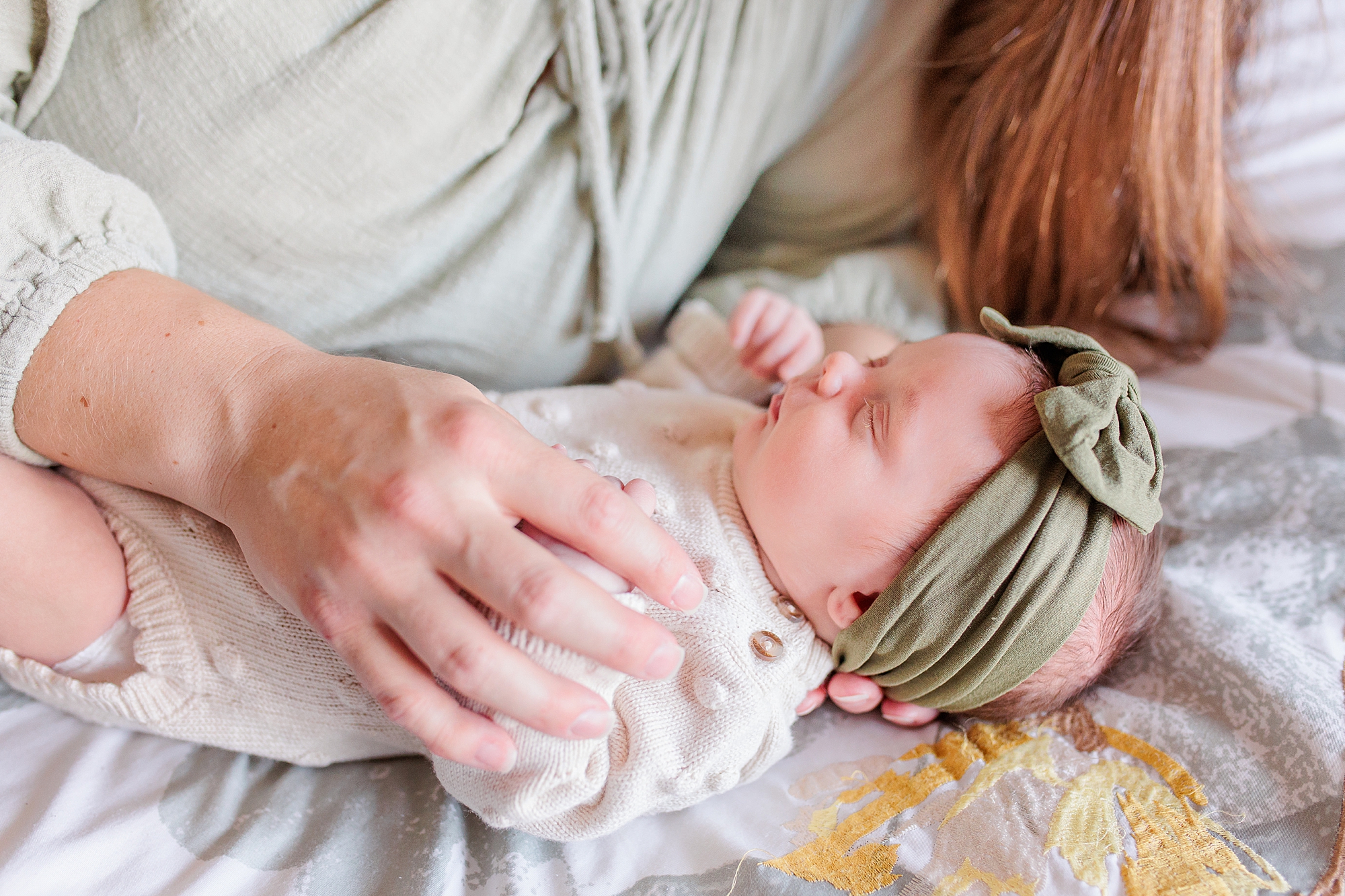mom holds newborn daughter next to her on bed during Maryland newborn lifestyle photos