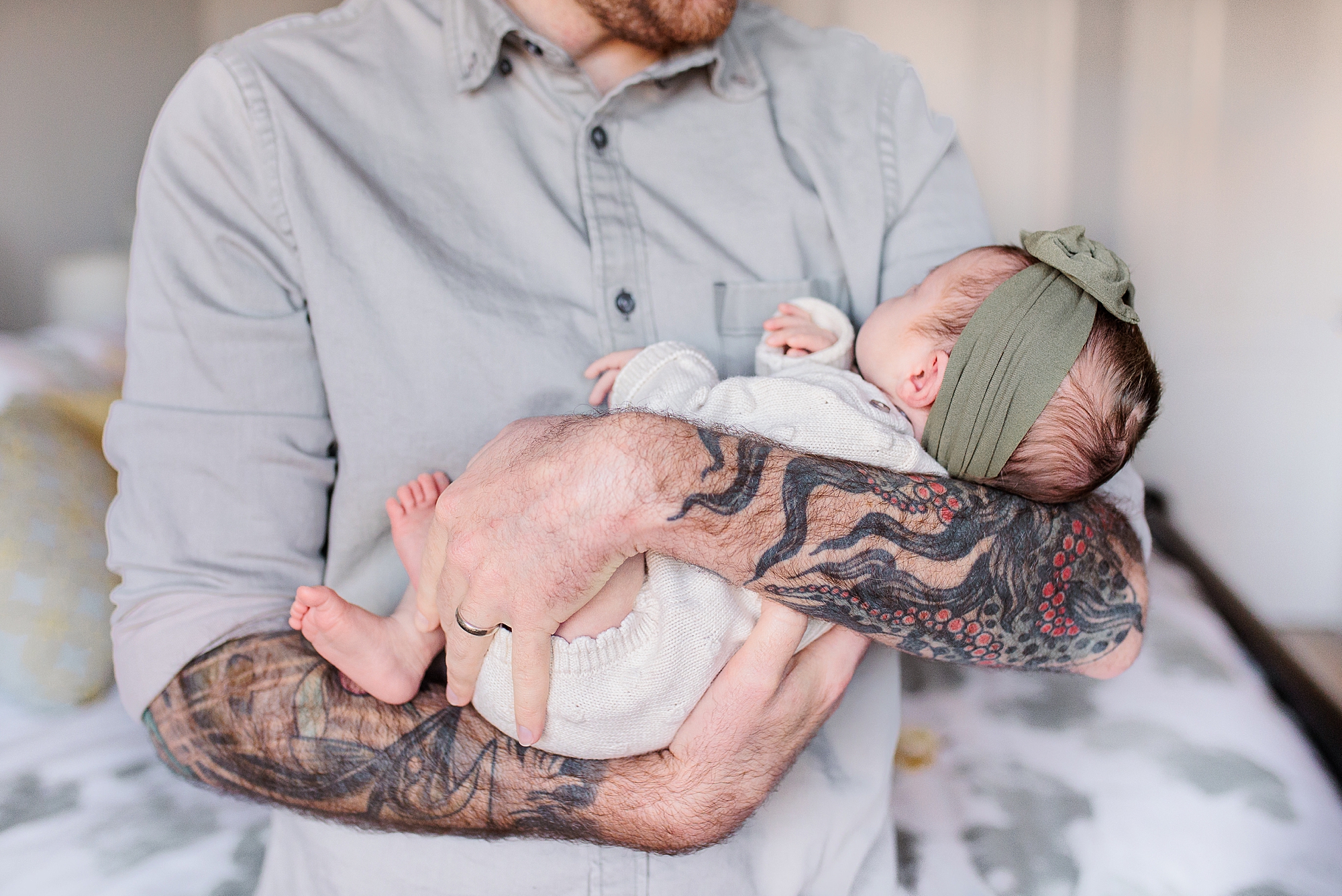 dad with tattooed arms snuggles newborn daughter in arms 
