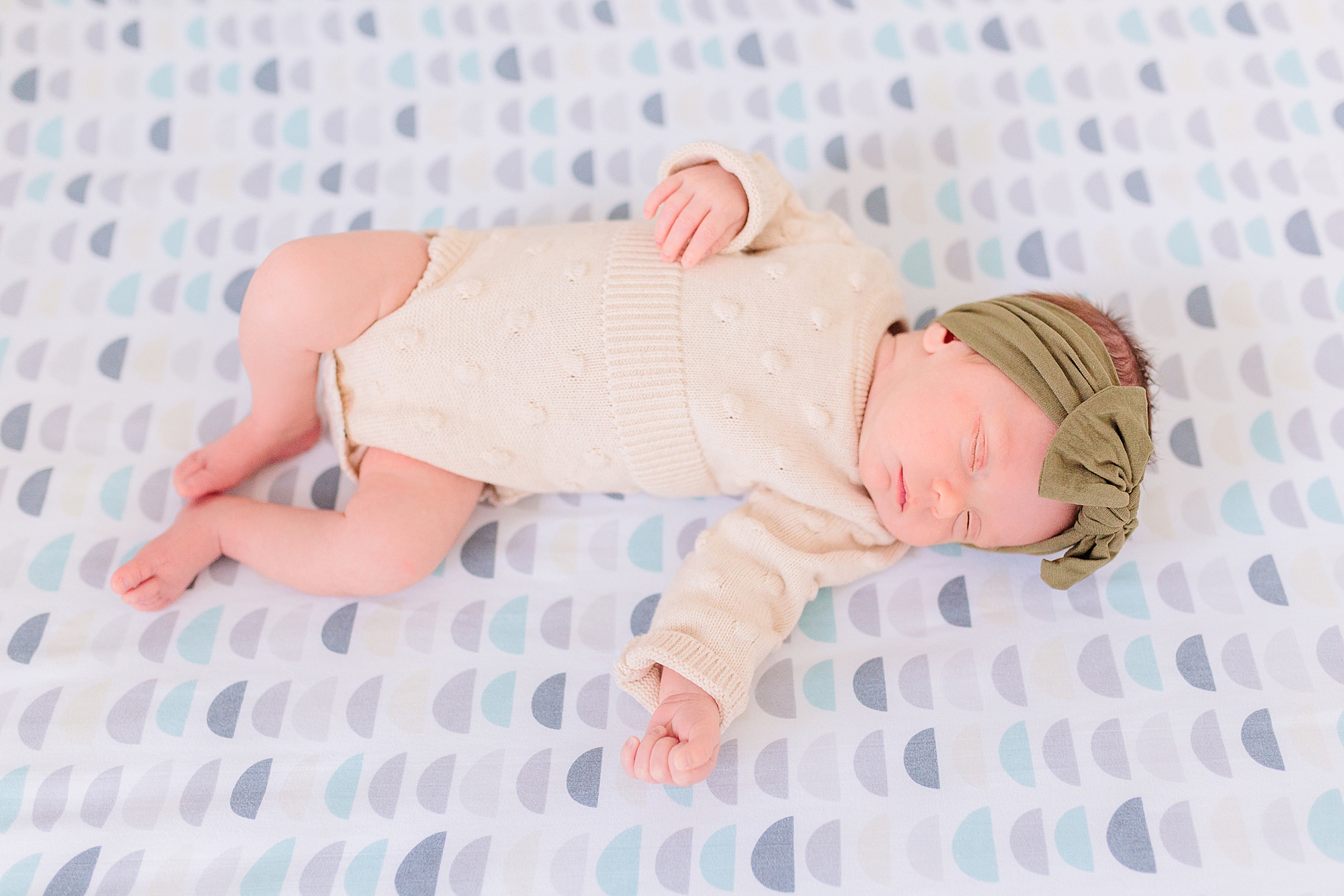baby girl in white onesie with green headband lays on nautical inspired crib sheets 