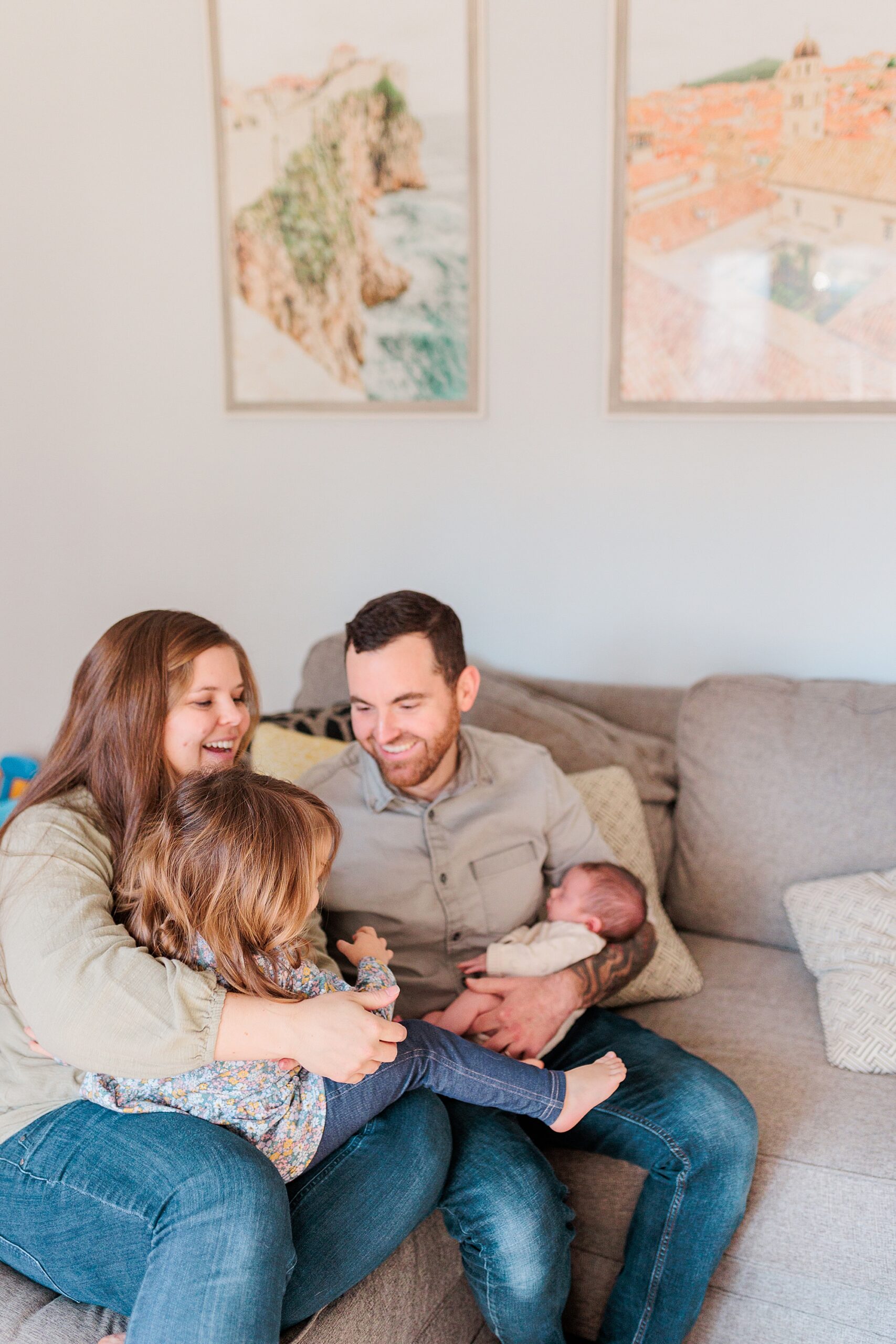 parents snuggle with two daughters on couch during Maryland newborn lifestyle photos