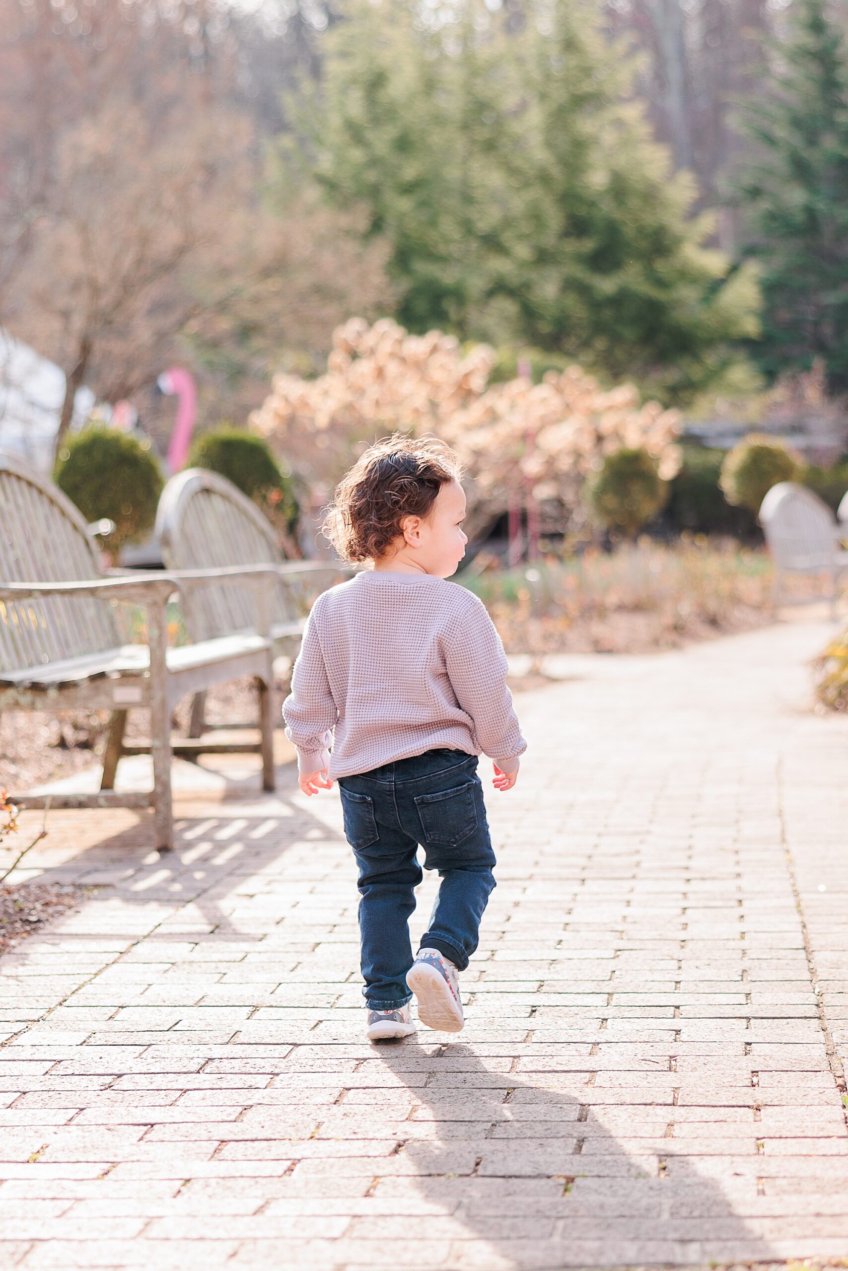child in pink sweater walks on brick pathway
