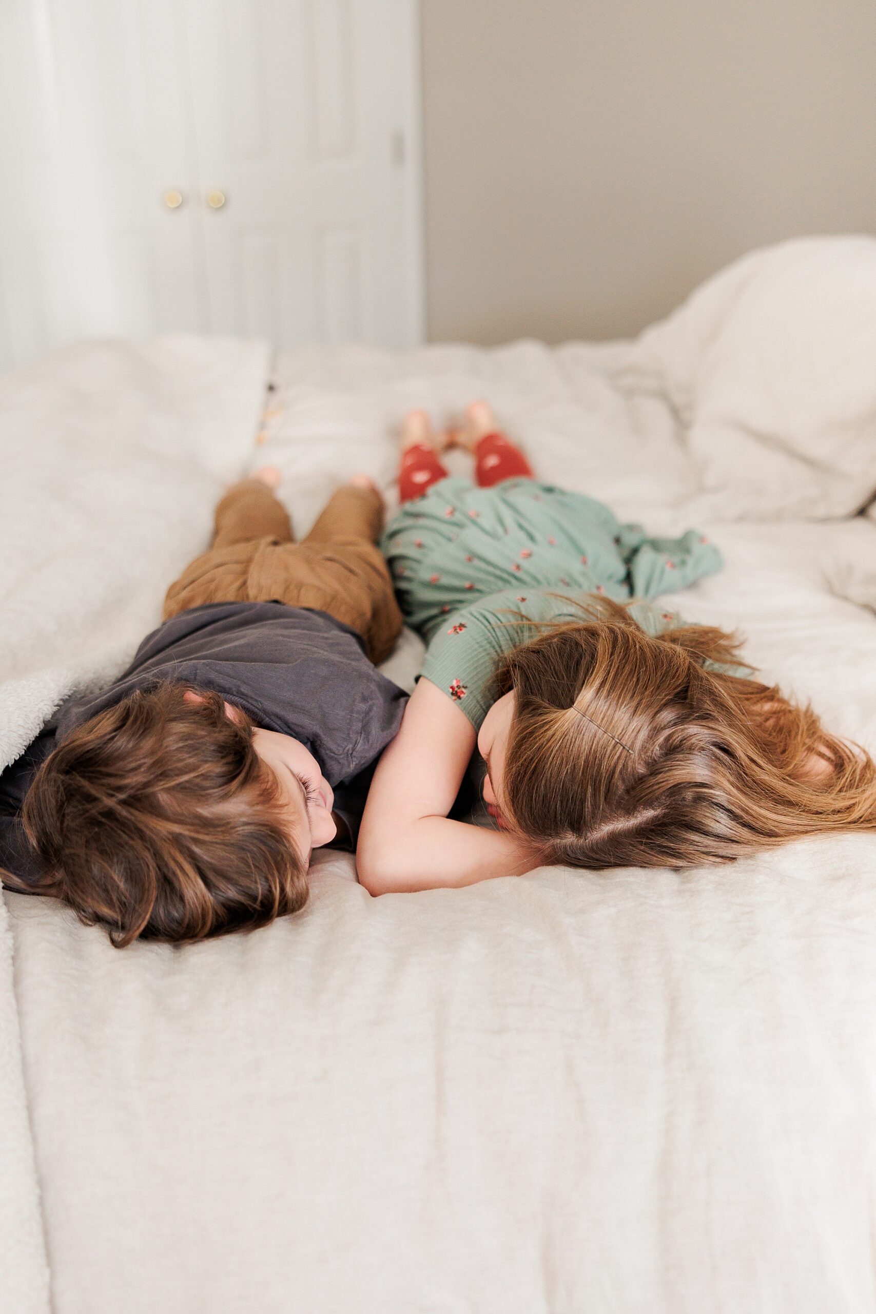 two kids lay facing each other on bed during Baltimore in-home family photos