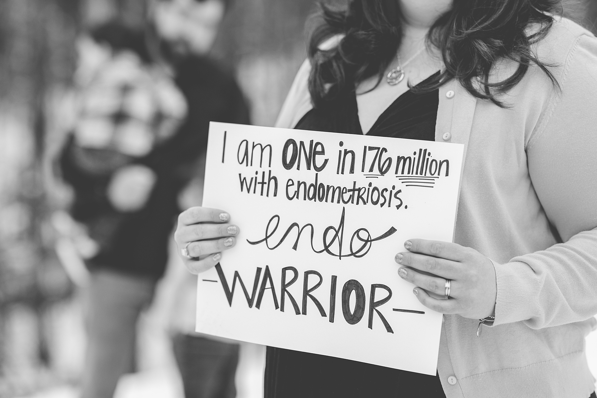 woman holds black and white sign that says "I am one in 176 million with Endometriosis"
