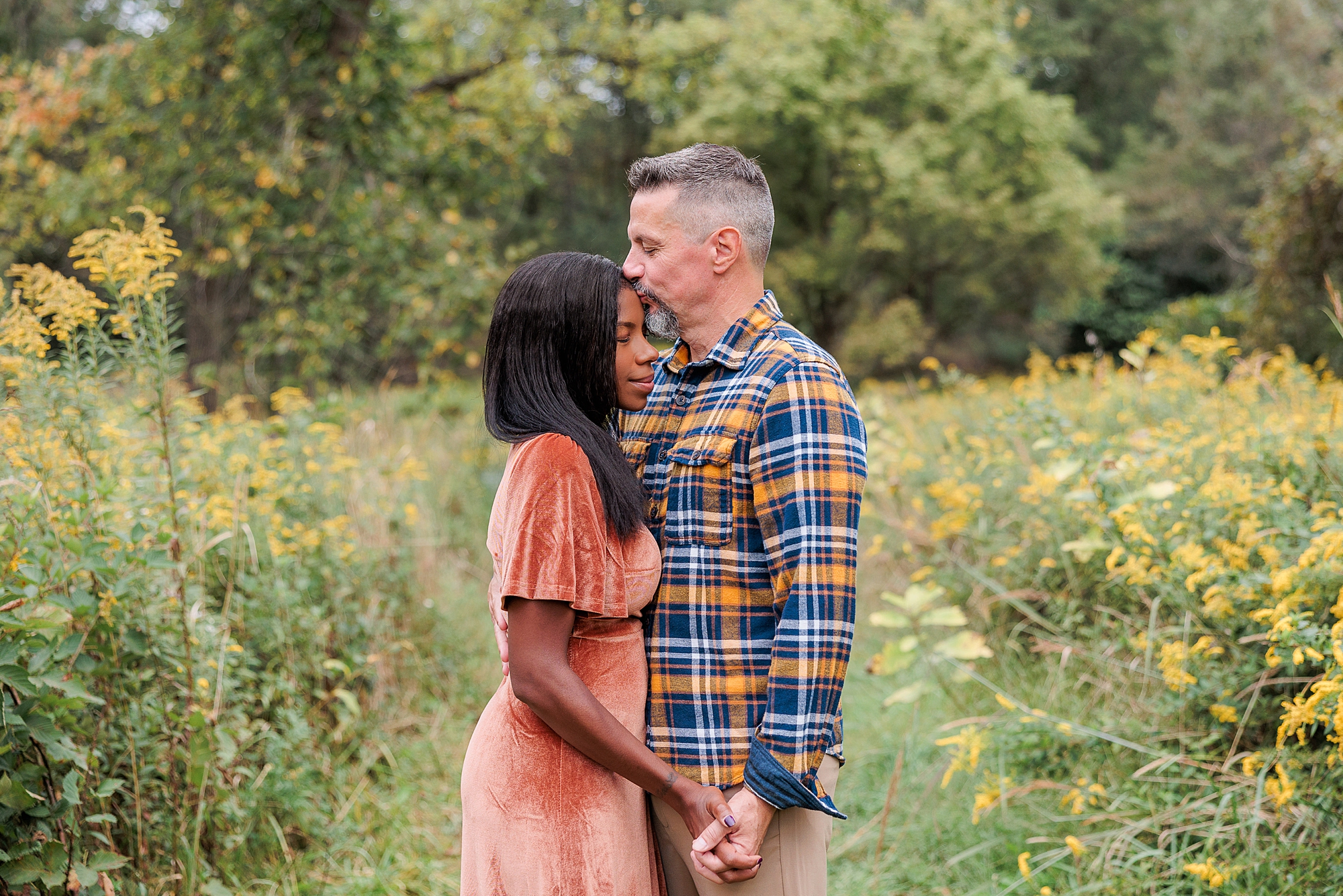 husband kisses wife's forehead during fall family photos 