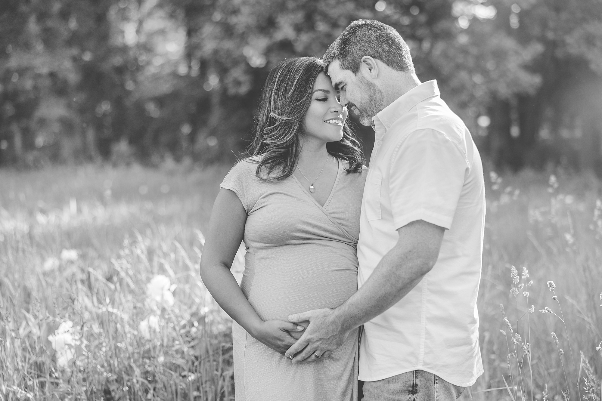 husband leans head into wife's forehead while holding her baby bump at Seneca Creek Park
