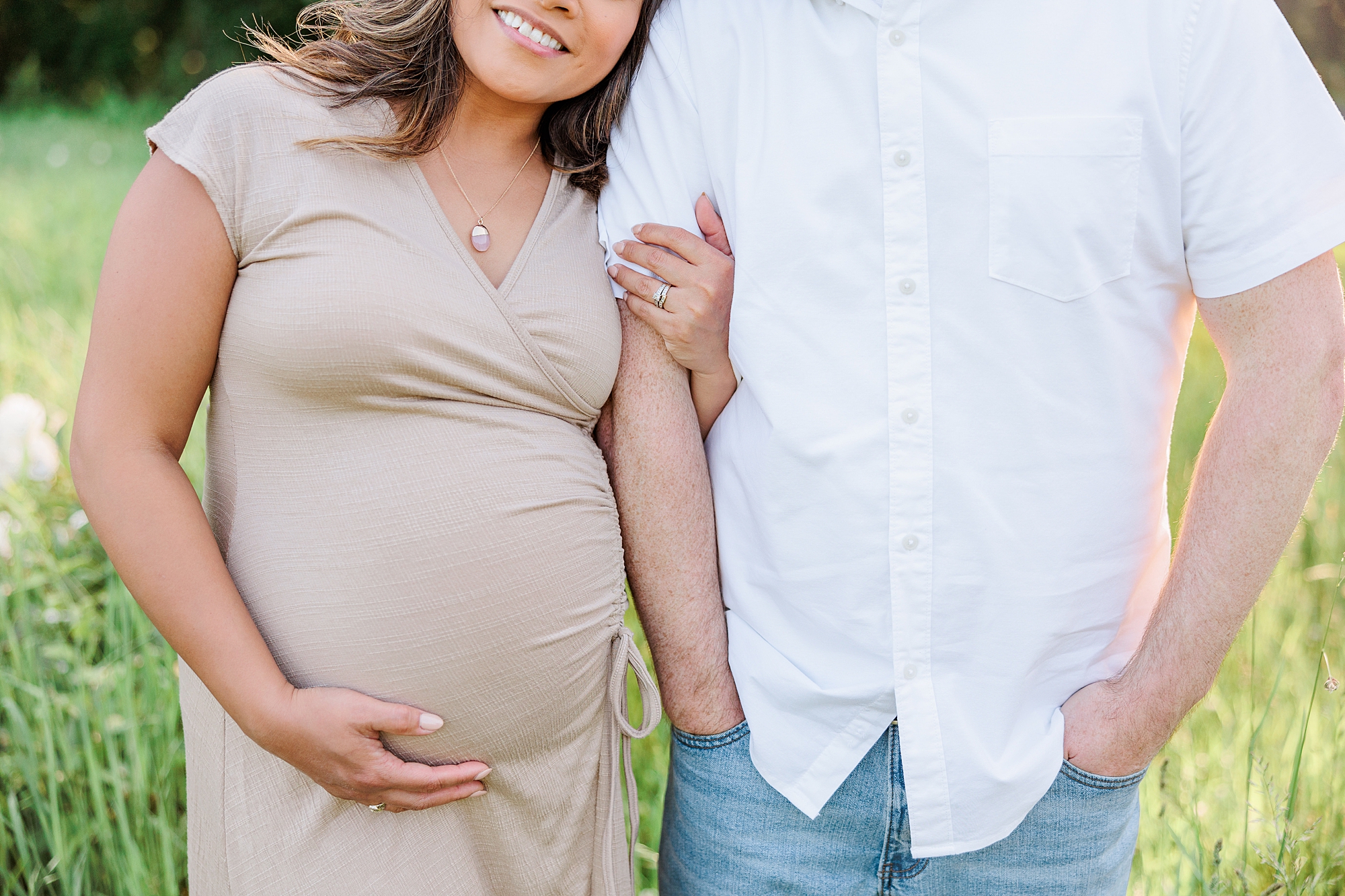 woman holds husband's arm and baby bump leaning on his shoulder during Seneca Creek Park maternity photos