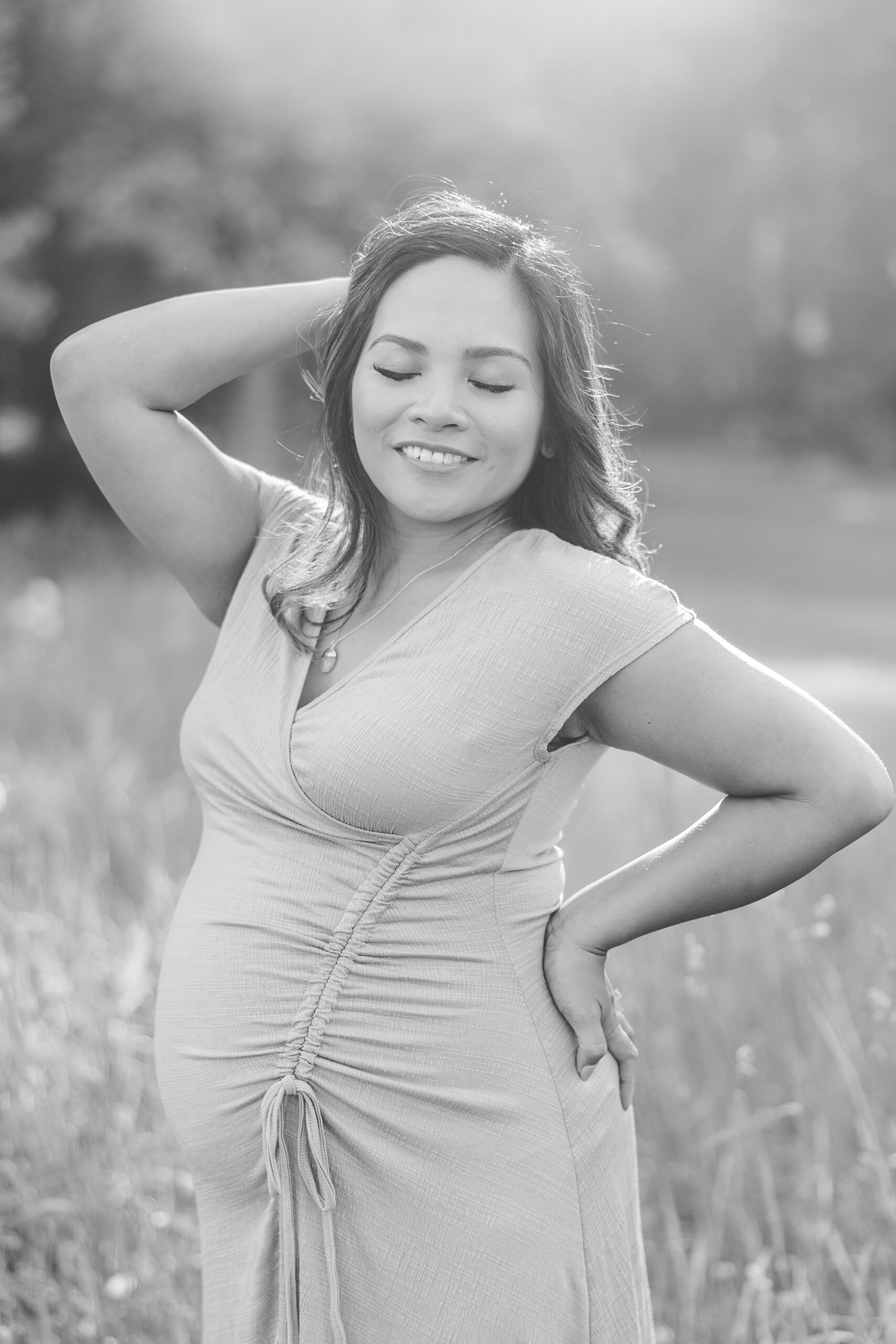 black and white photo of woman pushing hair back while holding back during maternity photos