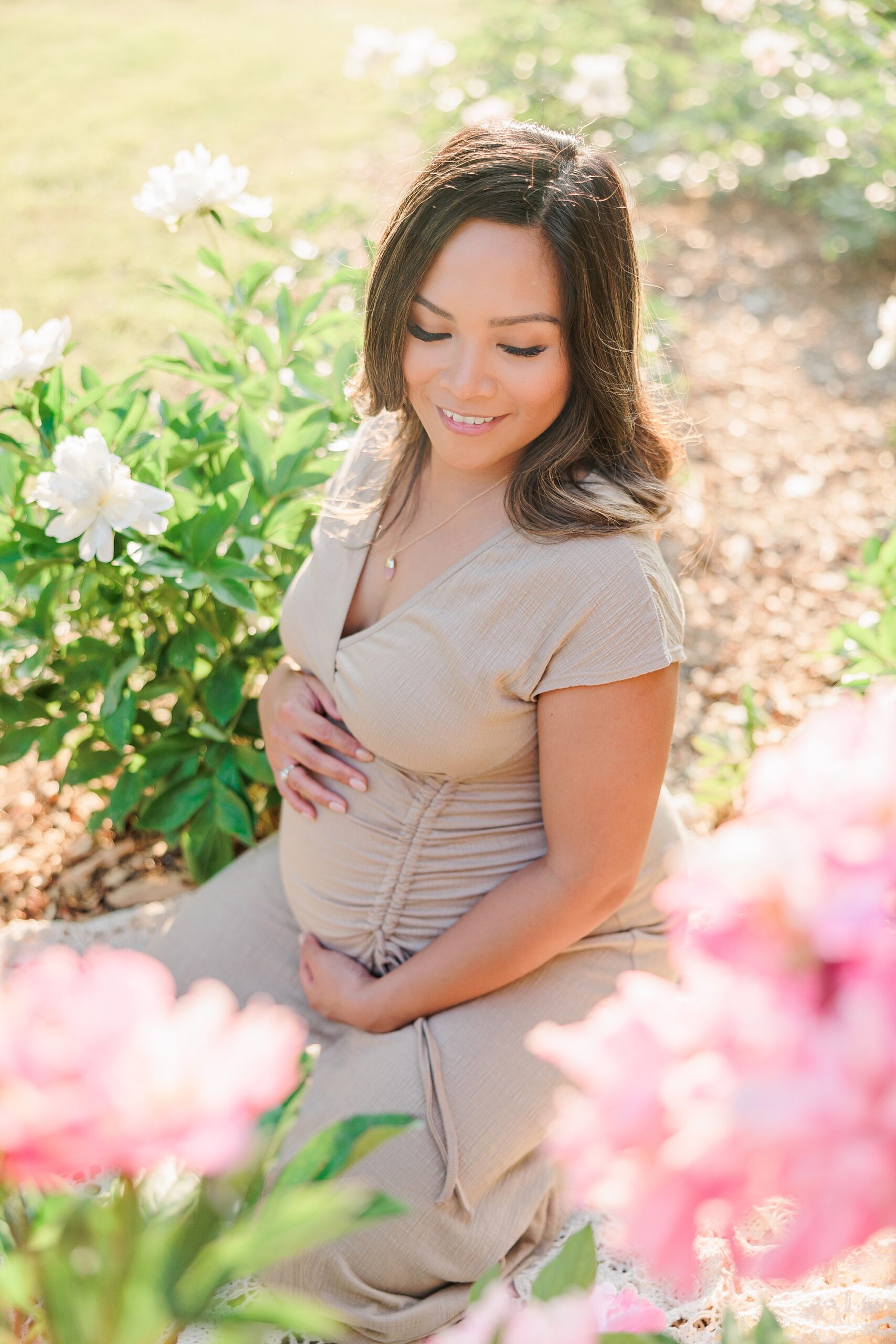 expecting mother sits among pink peonies at Seneca Creek Park