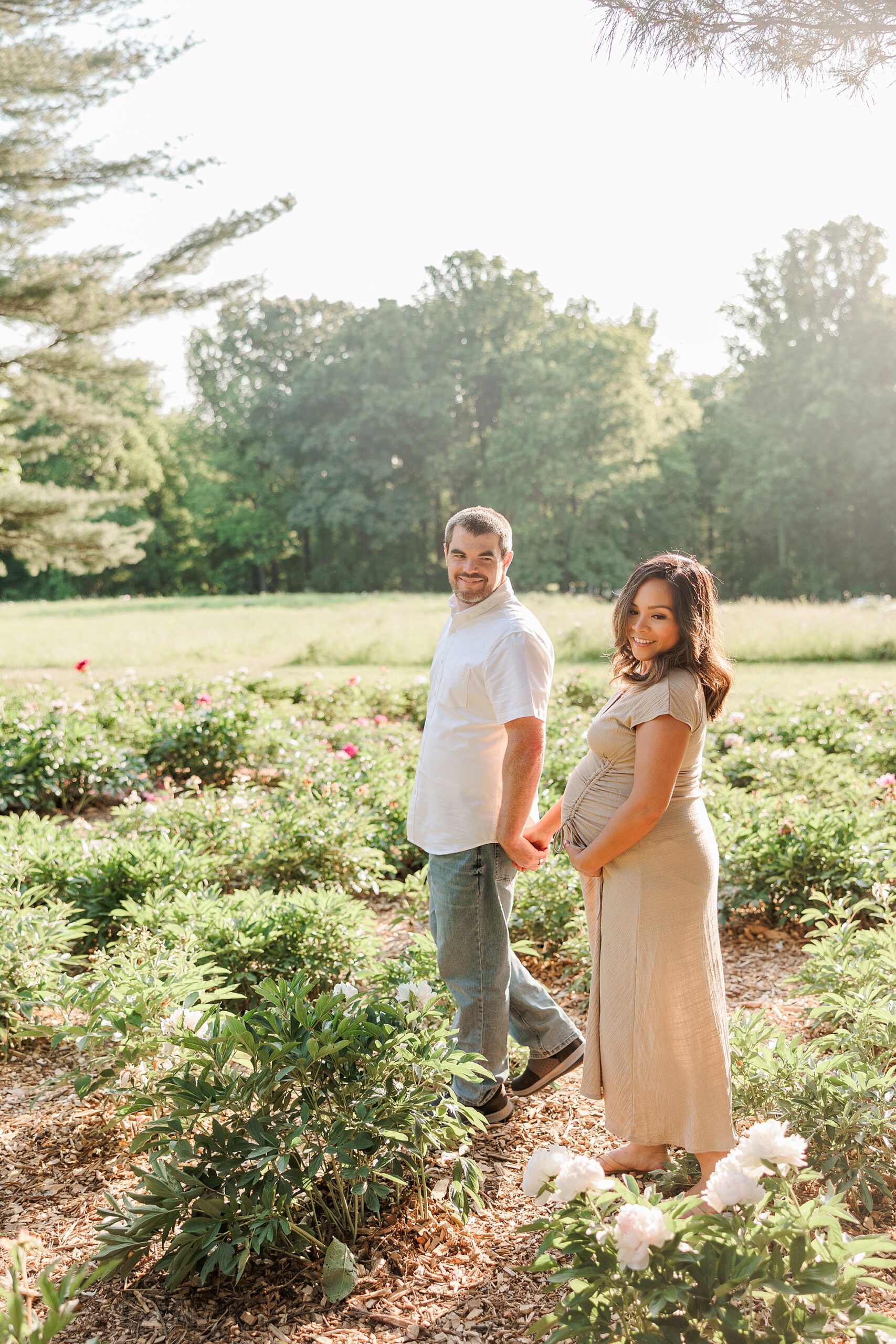 expecting couple holds hands walking through garden at Seneca Creek Park