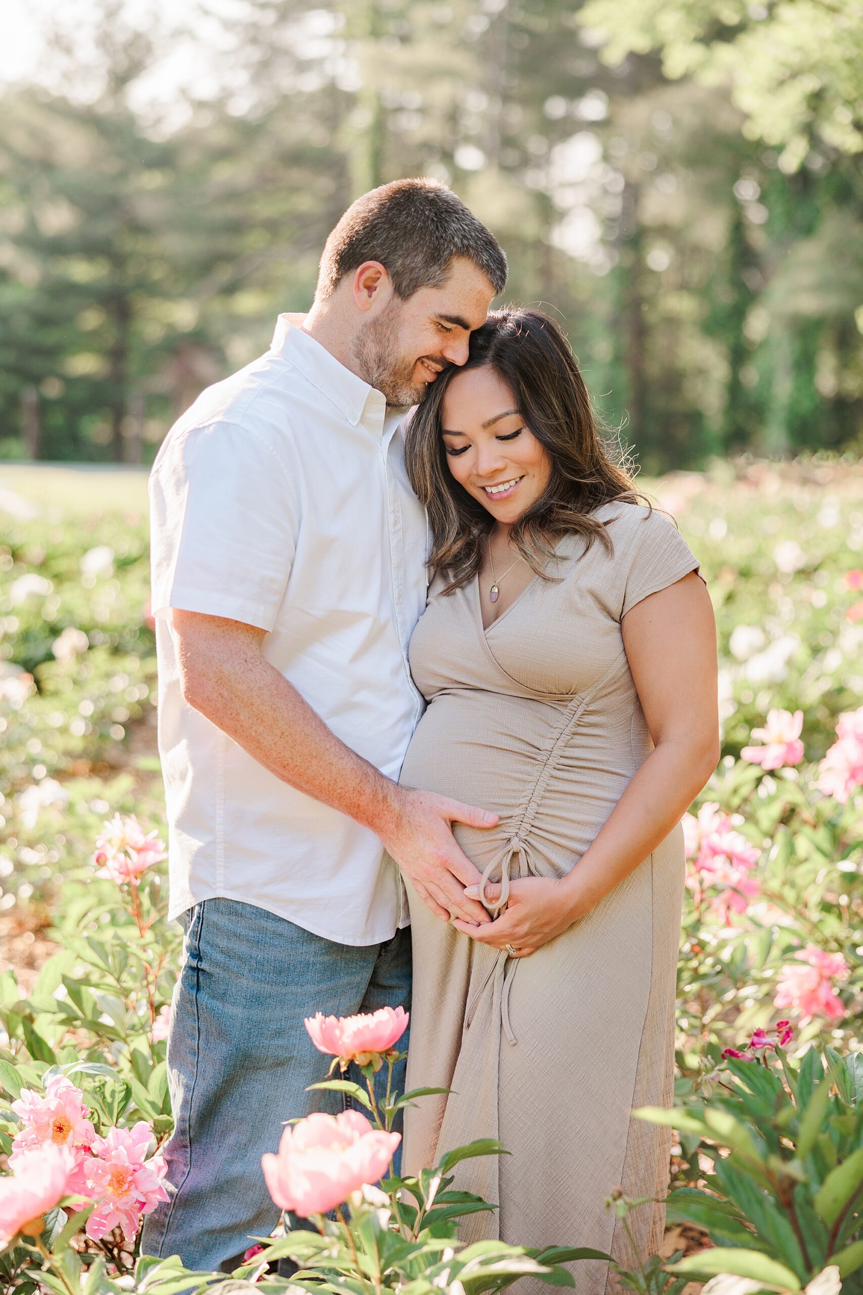 couple smiles hugging and holding mom's baby bump in garden at Seneca Creek Park