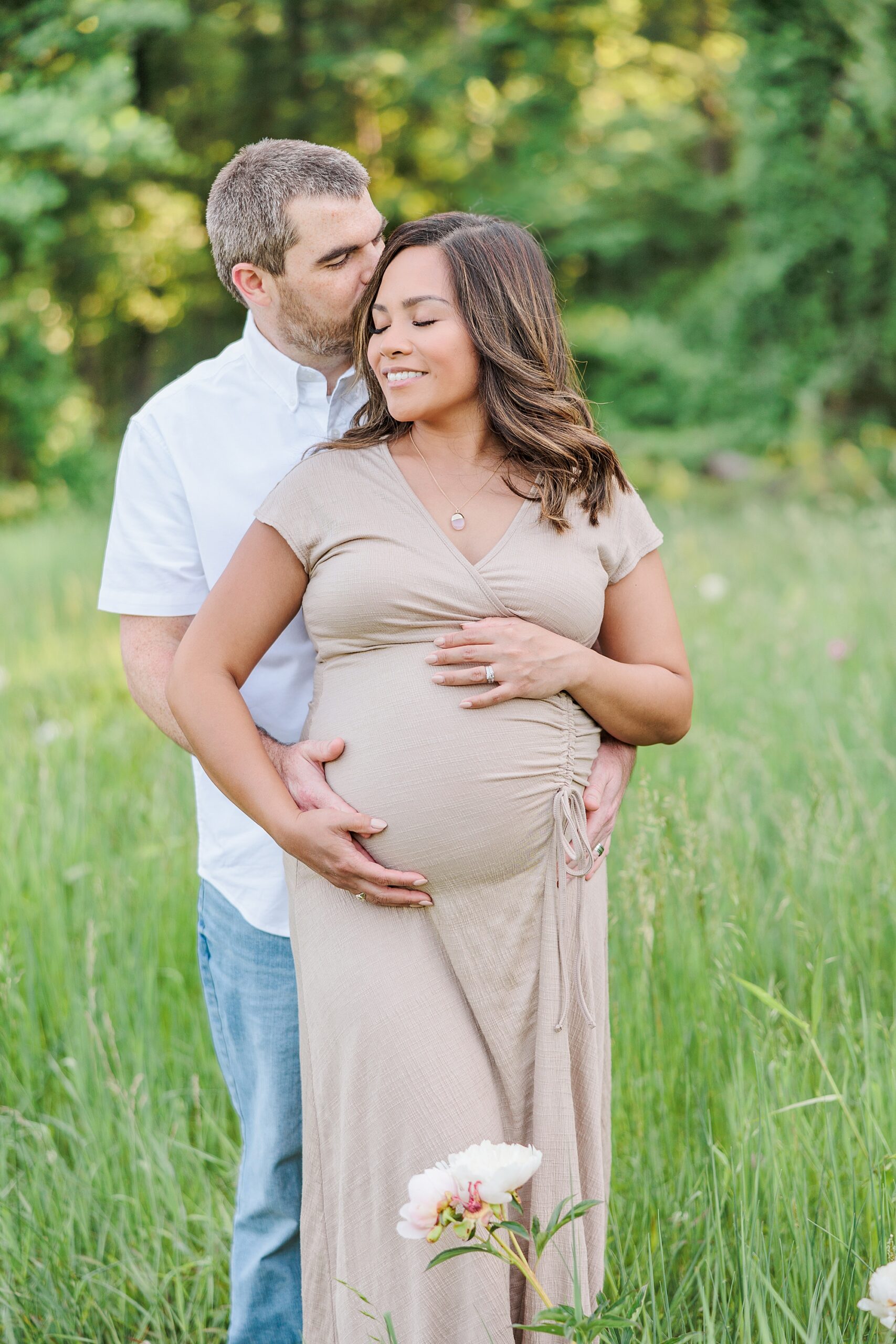 man stands behind wife hugging her and holding her baby bump
