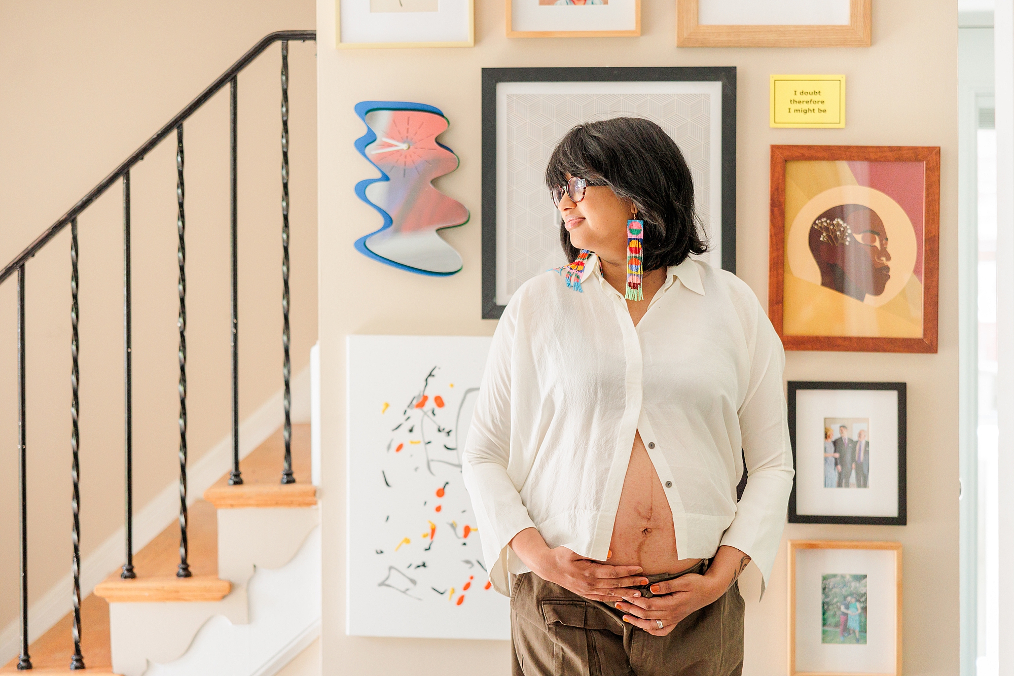 mom in white button up shirt holds baby bump in front of art display during Silver Spring Maternity lifestyle photos