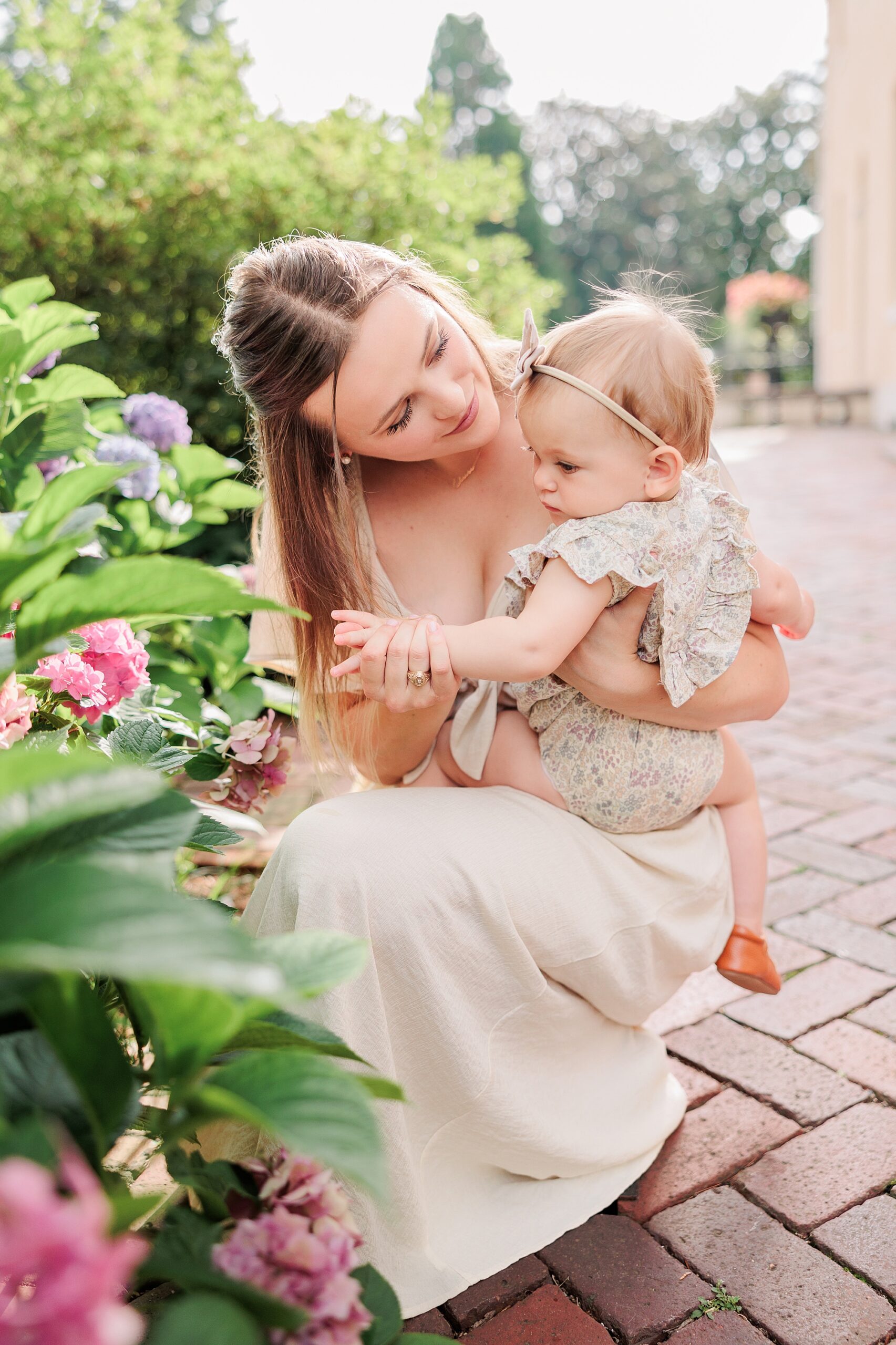mom kneels down with daughter on her hip by pink flowers