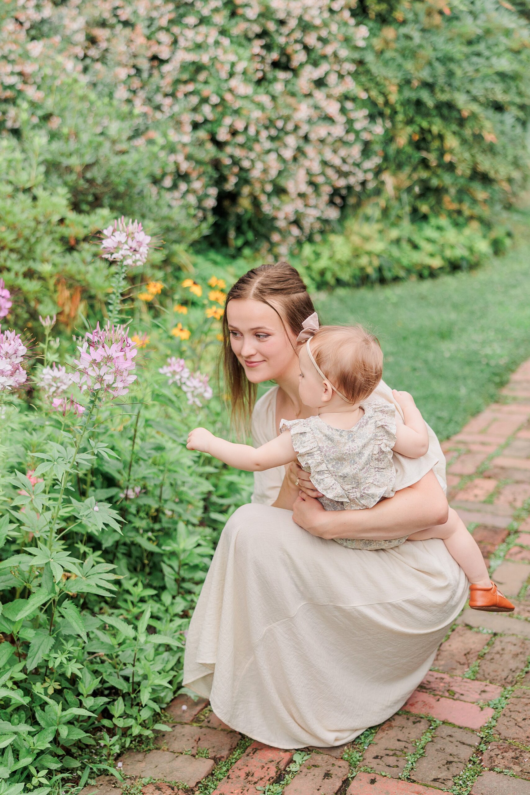 mom kneels down with daughter to look at pink flowers at Tudor Place