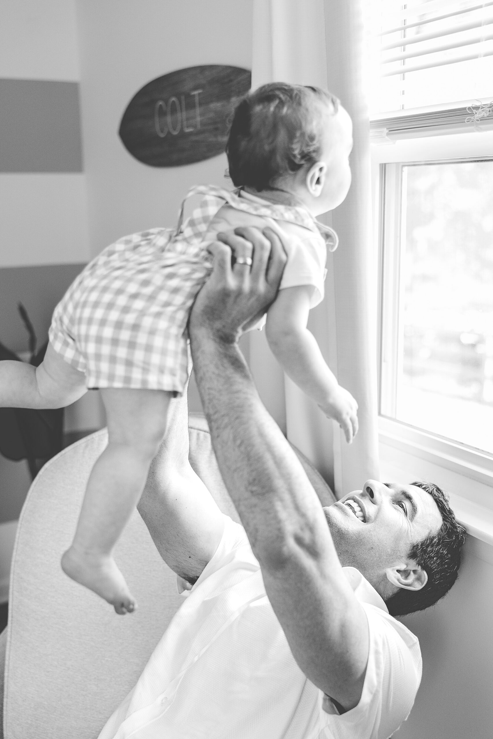 dad lifts up son looking out the window on couch during Maryland Family Lifestyle Photos