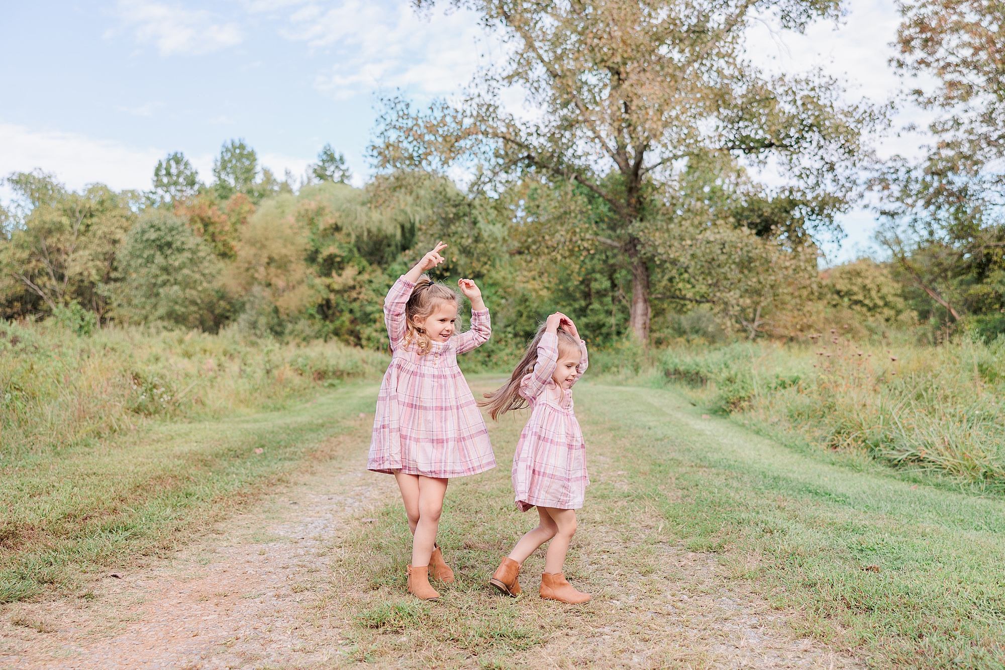 two girls in plaid pink dresses twirl on path in Northern Virginia